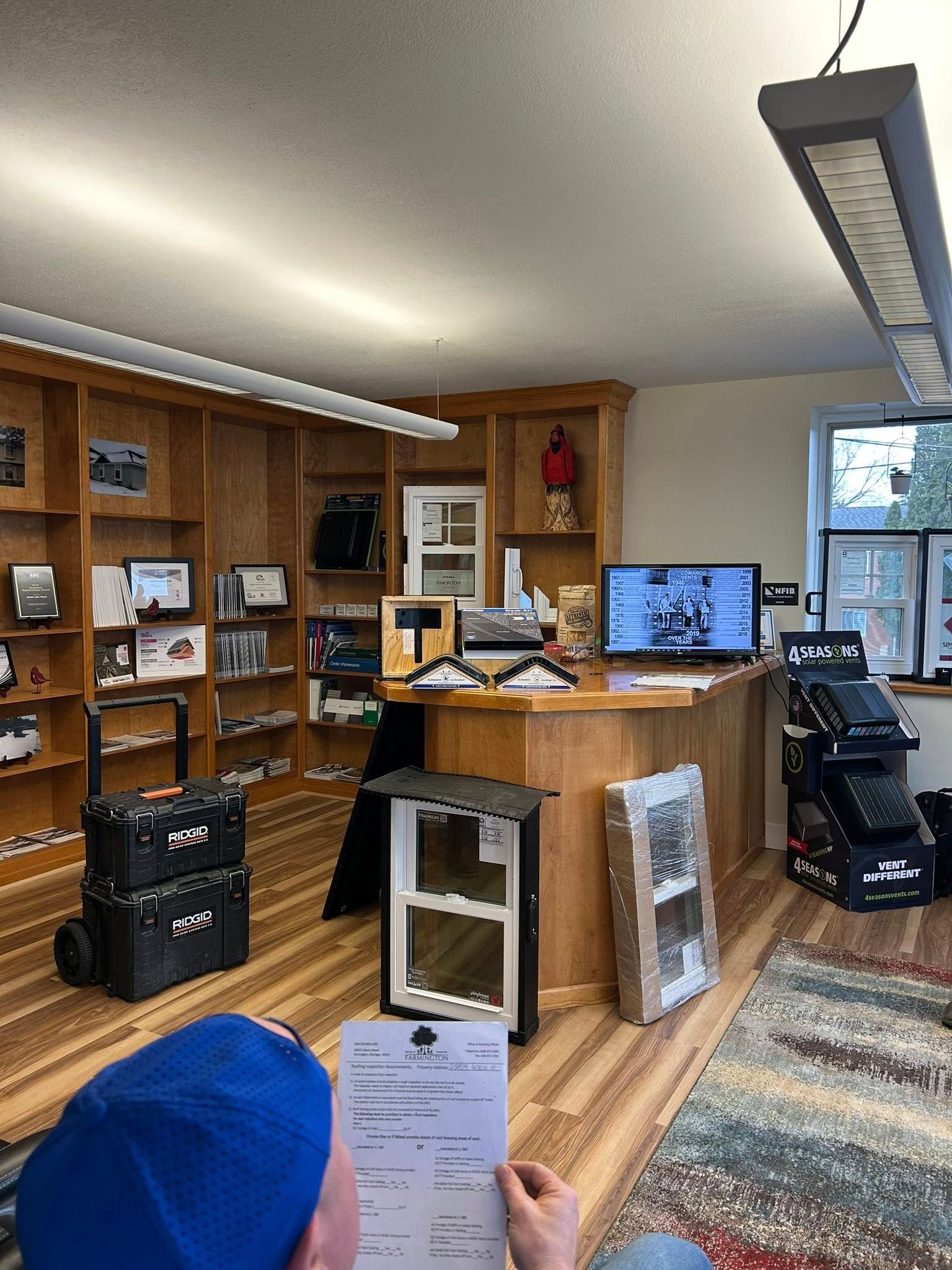 Indoor shop interior with wooden displays, shelves, counter, and monitors, viewed from the entrance.