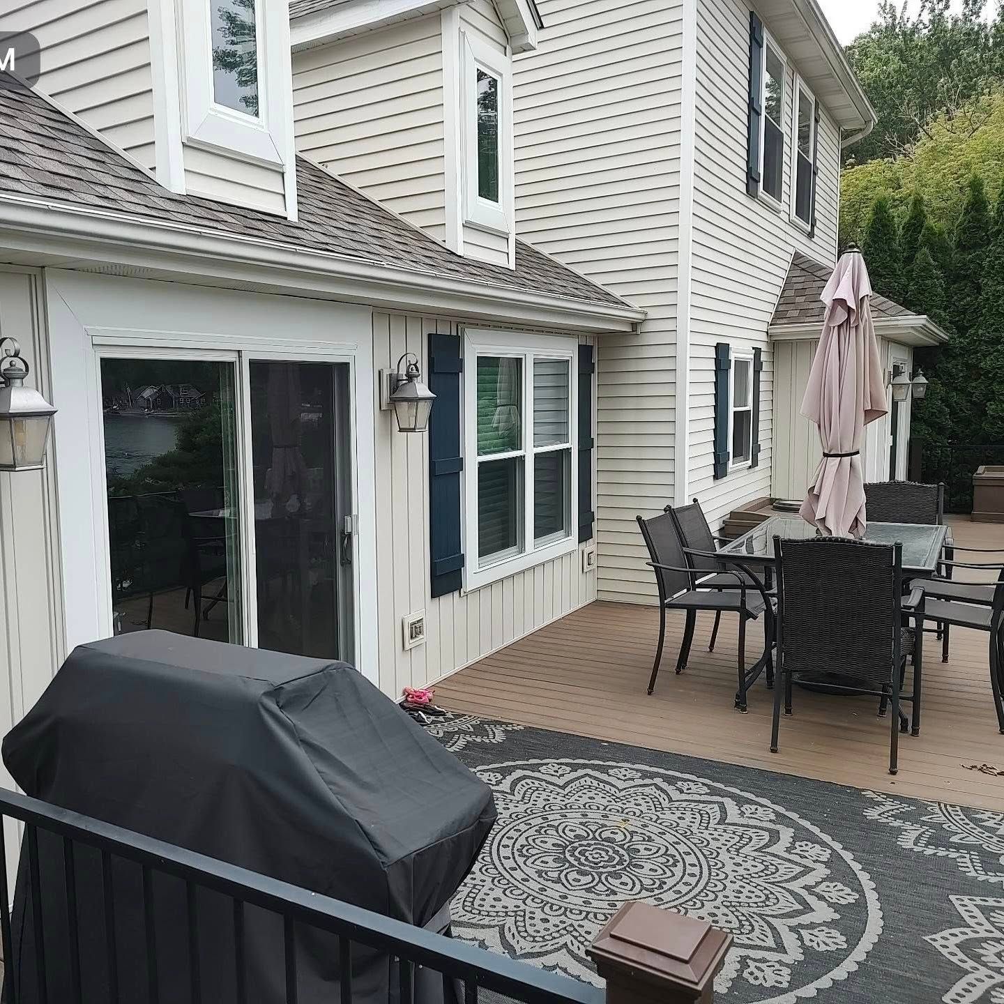 Back patio with grill, outdoor dining set, umbrella, and sliding glass doors beside a house
