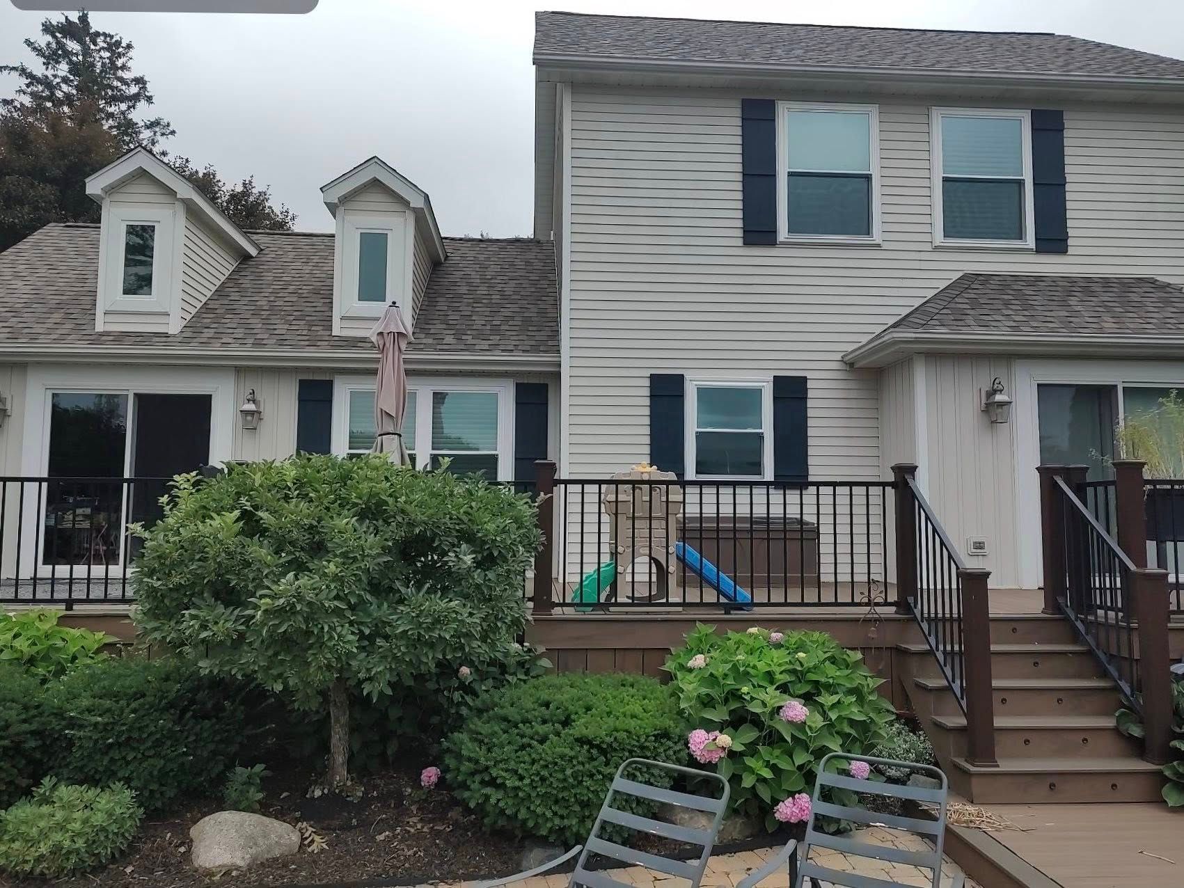 Two-story gray townhouse with front steps, porch, and flower bed under an overcast sky