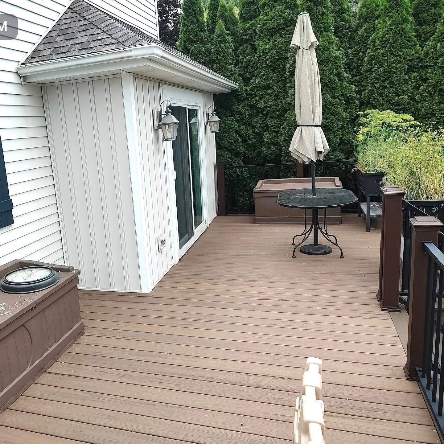 Wooden deck beside a white house, with a patio table, closed umbrella, and outdoor furniture.