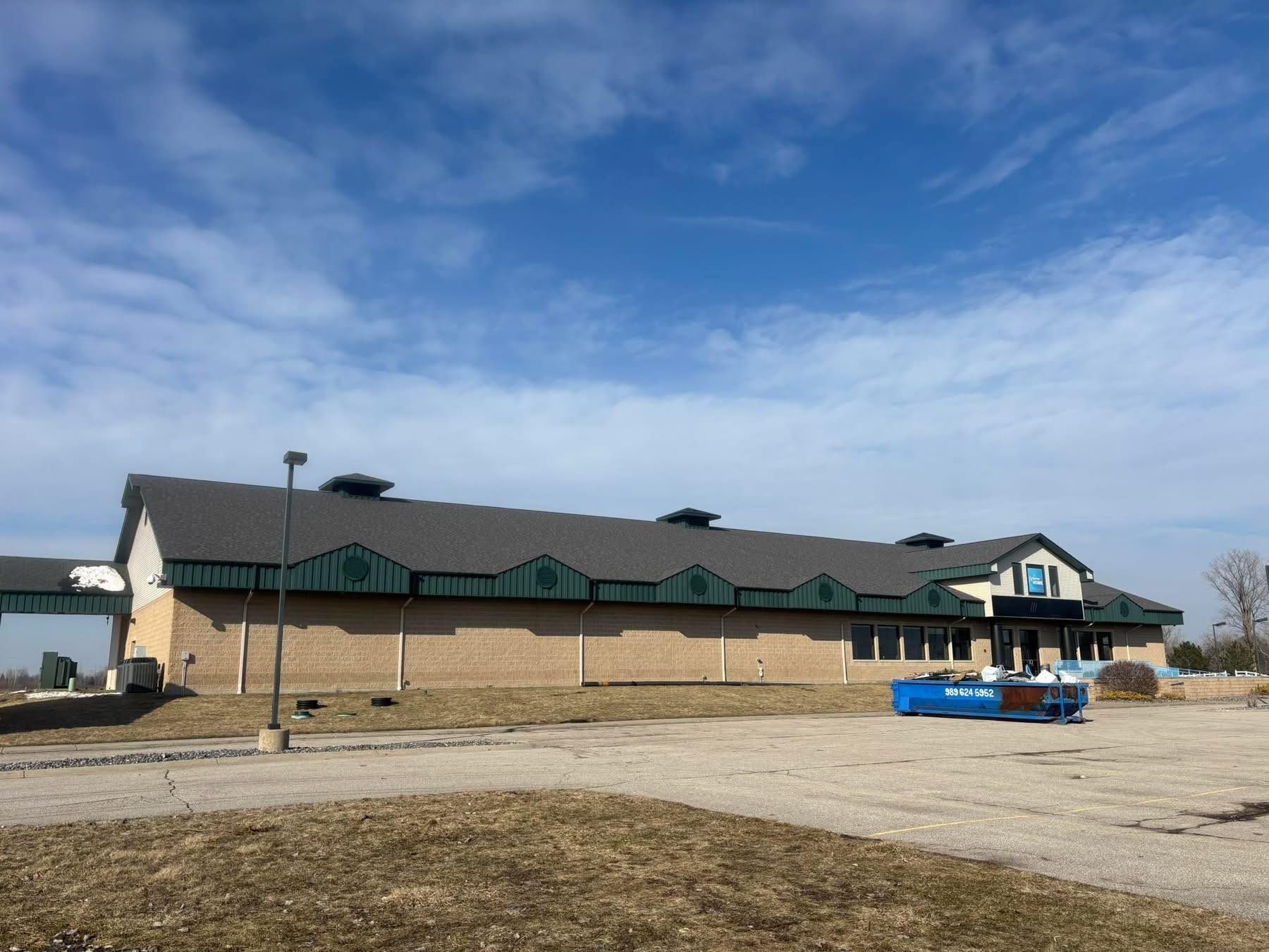Low brick building with green roof on a gravel lot under a blue sky