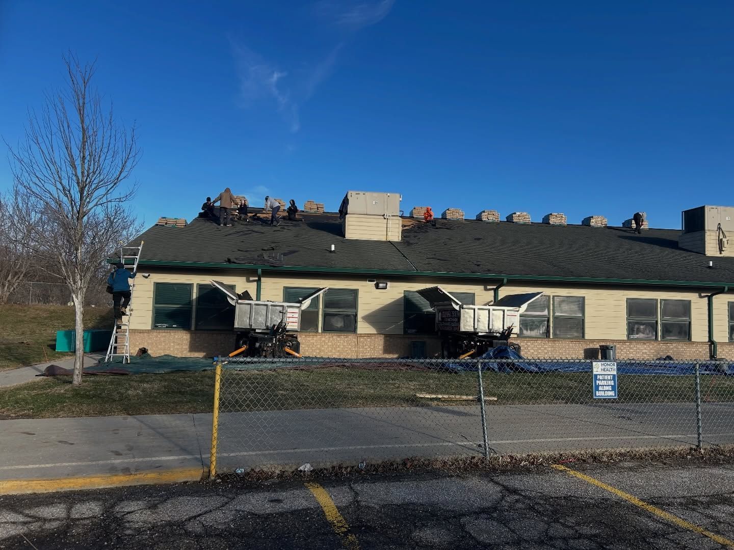 Single-story beige building with a dark roof, chain-link fence, and a clear blue sky.
