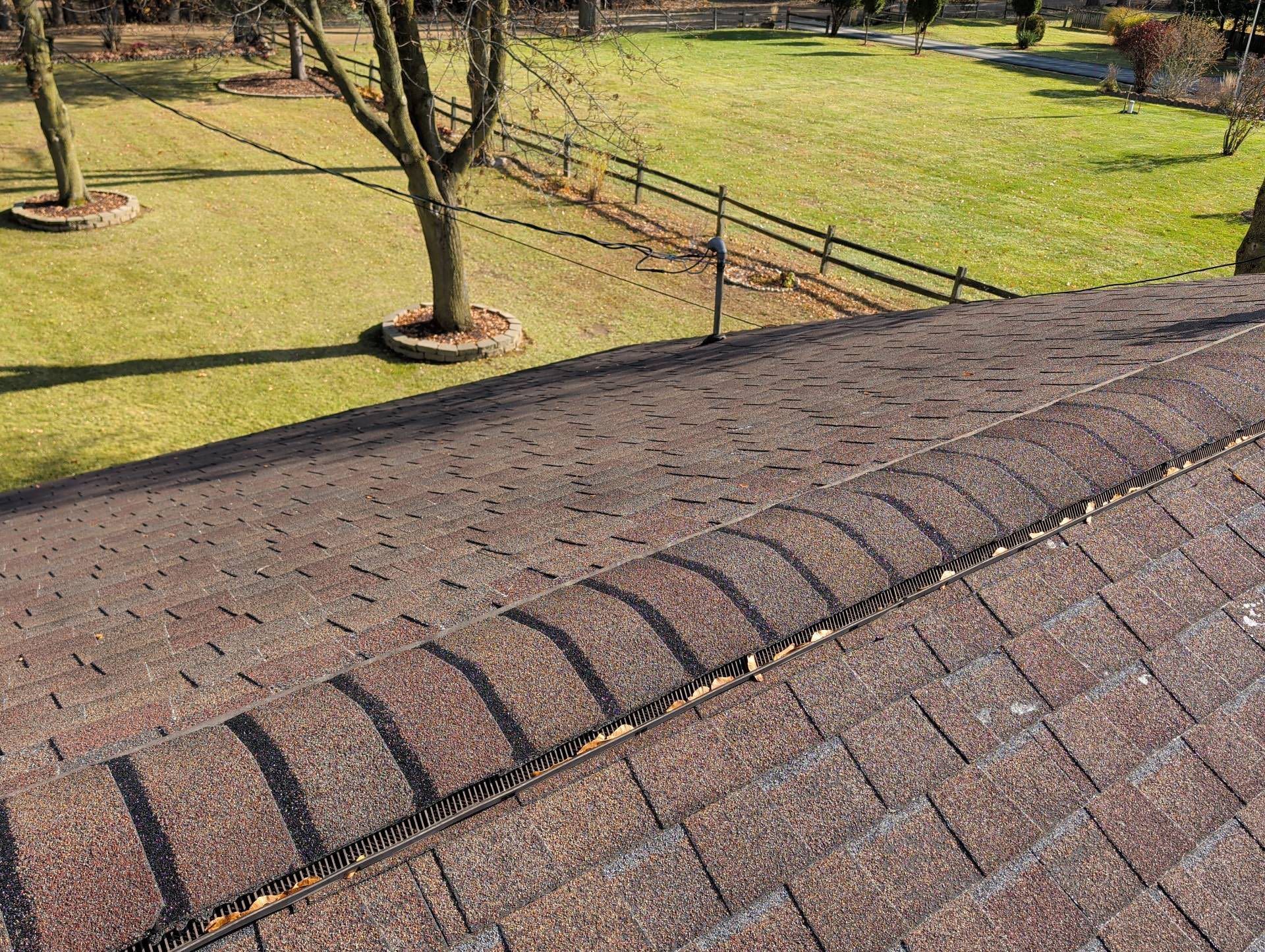 Rooftop shingles overlooking a grassy park with trees and a fence