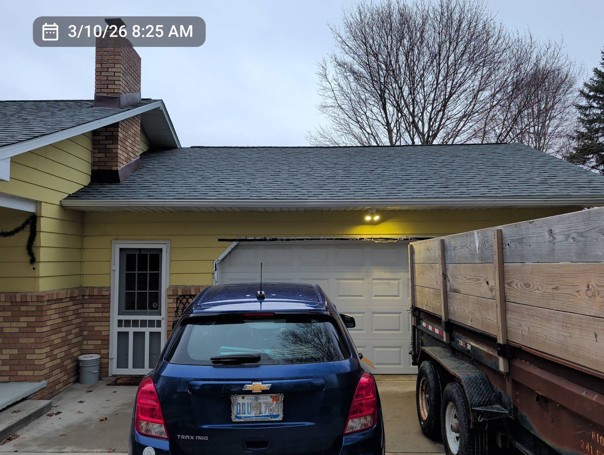Driveway with a dark blue car parked in front of a yellow house and closed garage at dusk.