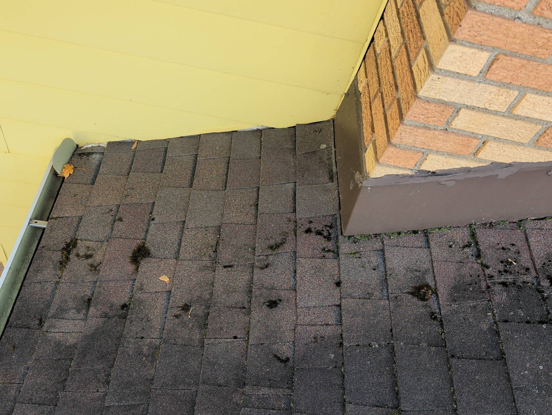 Roof shingles next to a yellow wall and brick chimney corner