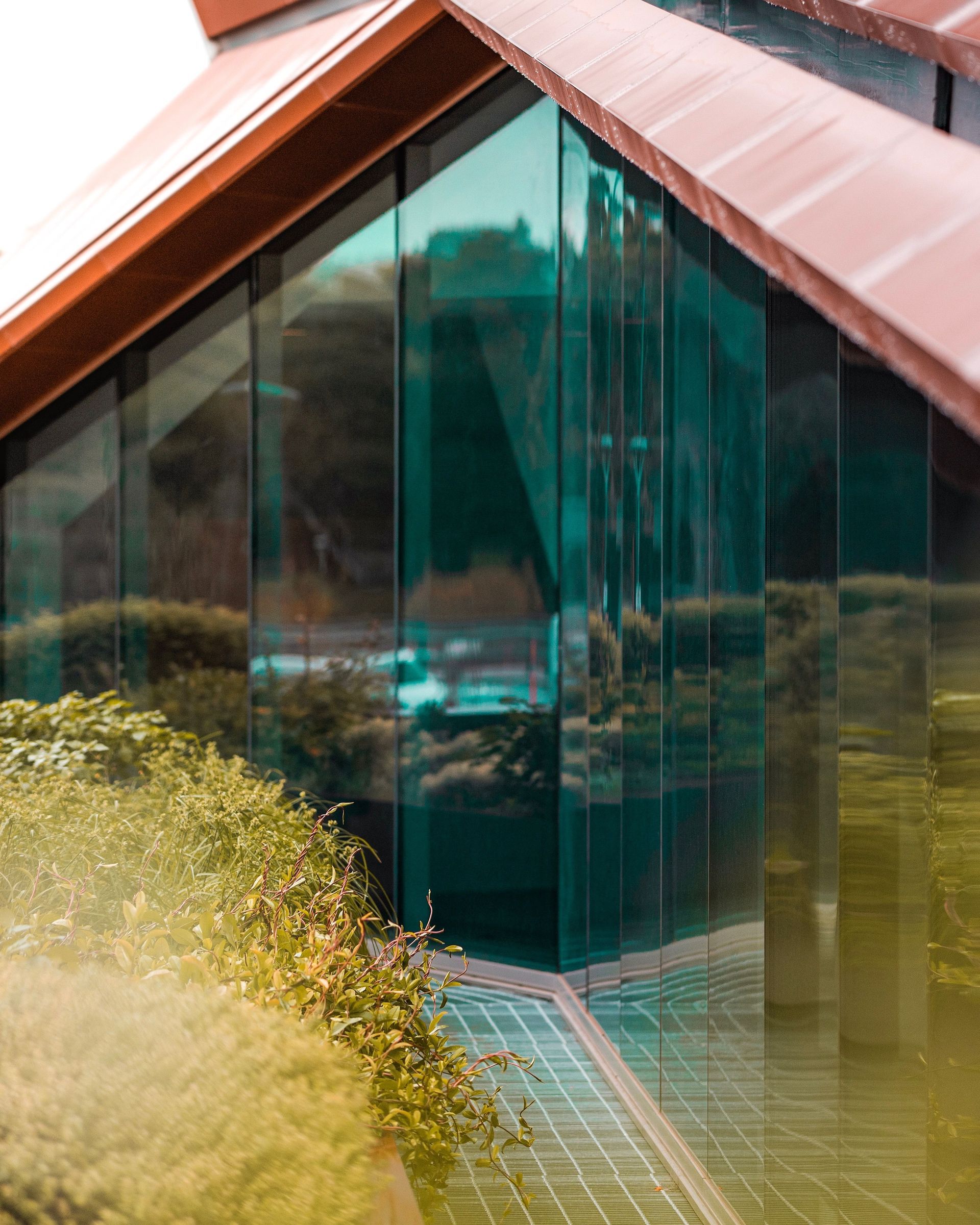 Modern house with large glass windows, red roof, and reflections of greenery in front