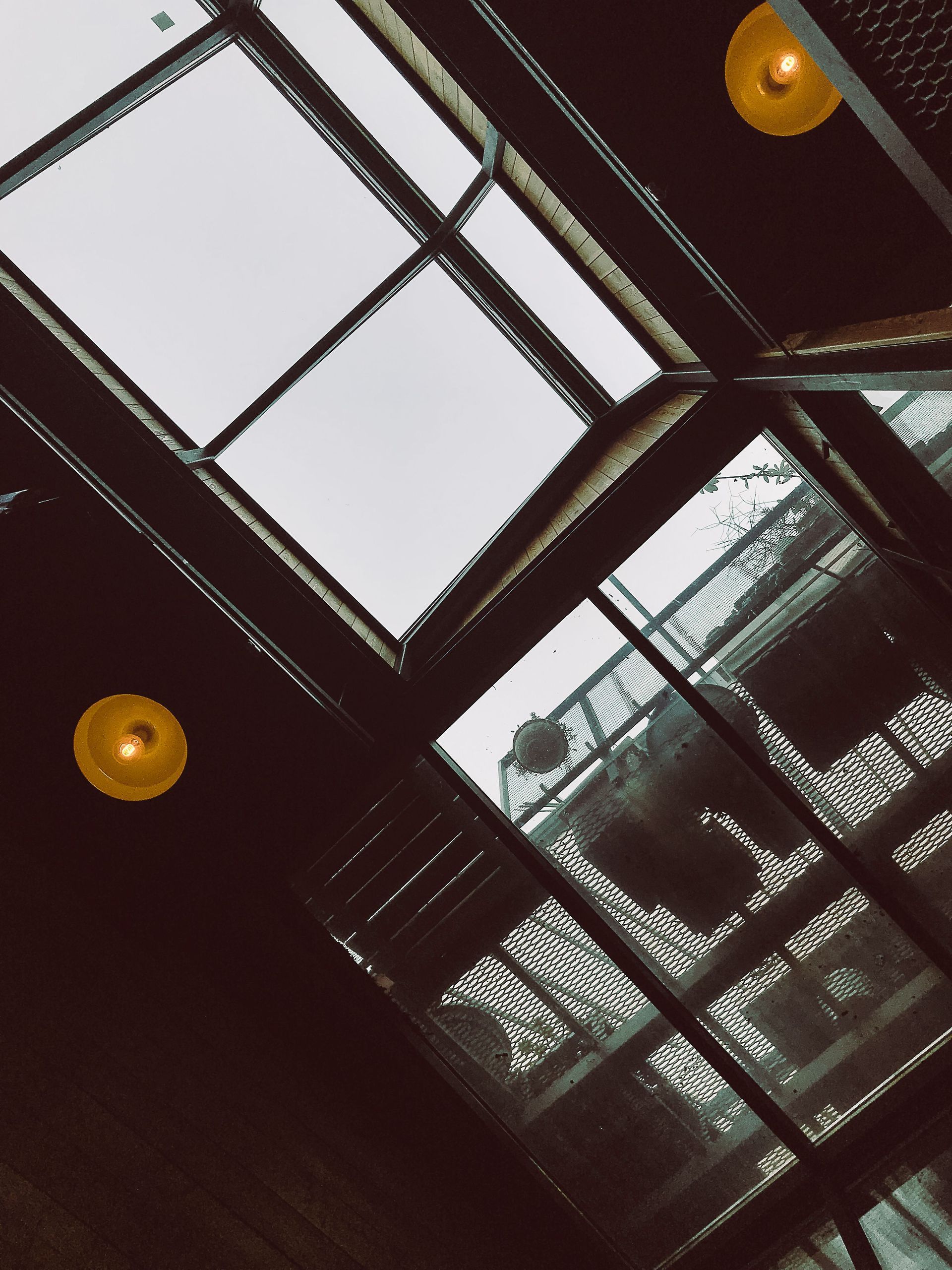Tilted view of a glass atrium ceiling with dark beams and warm round lights