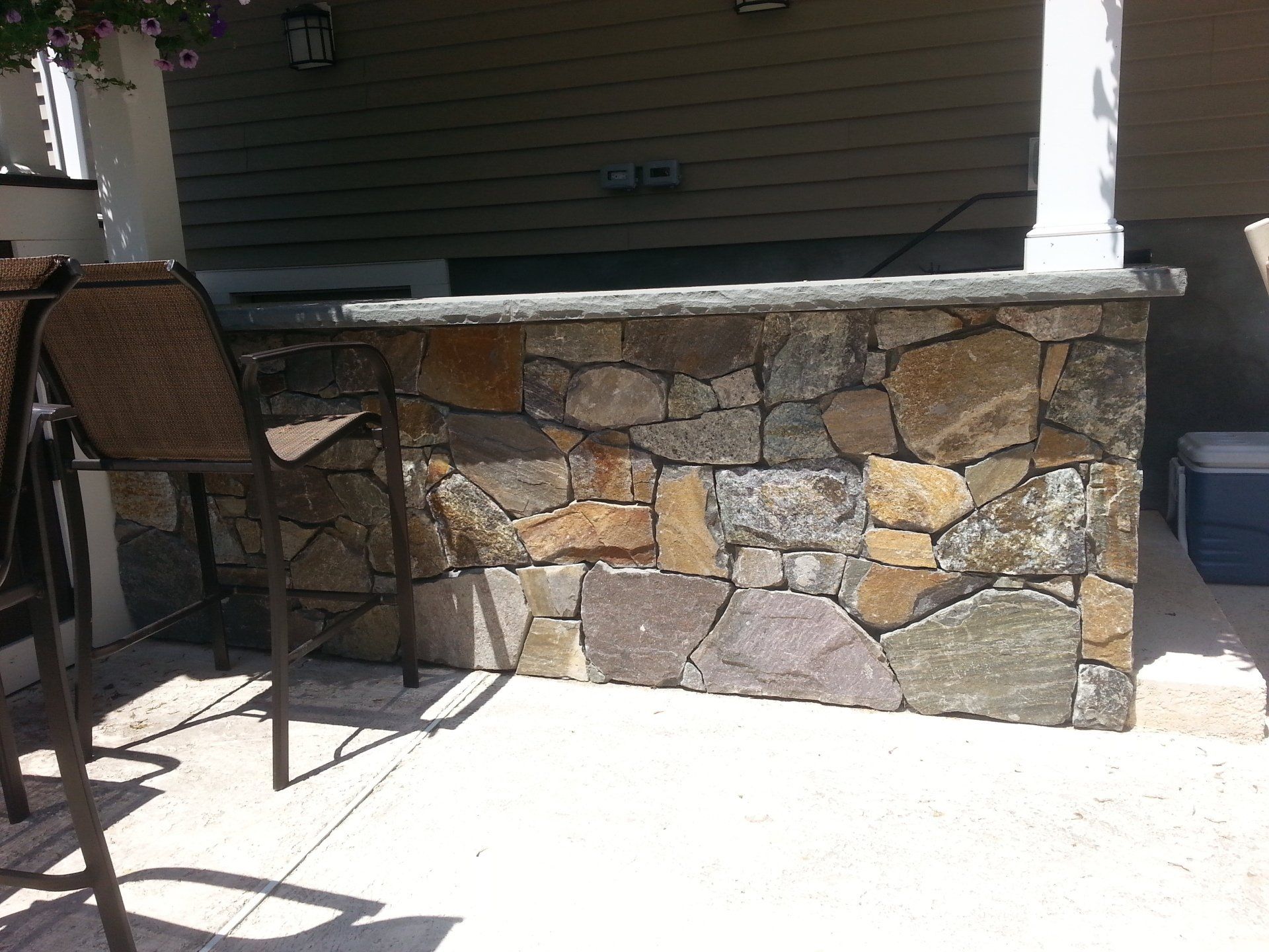 Stone outdoor bar with brown wicker chairs on a patio.
