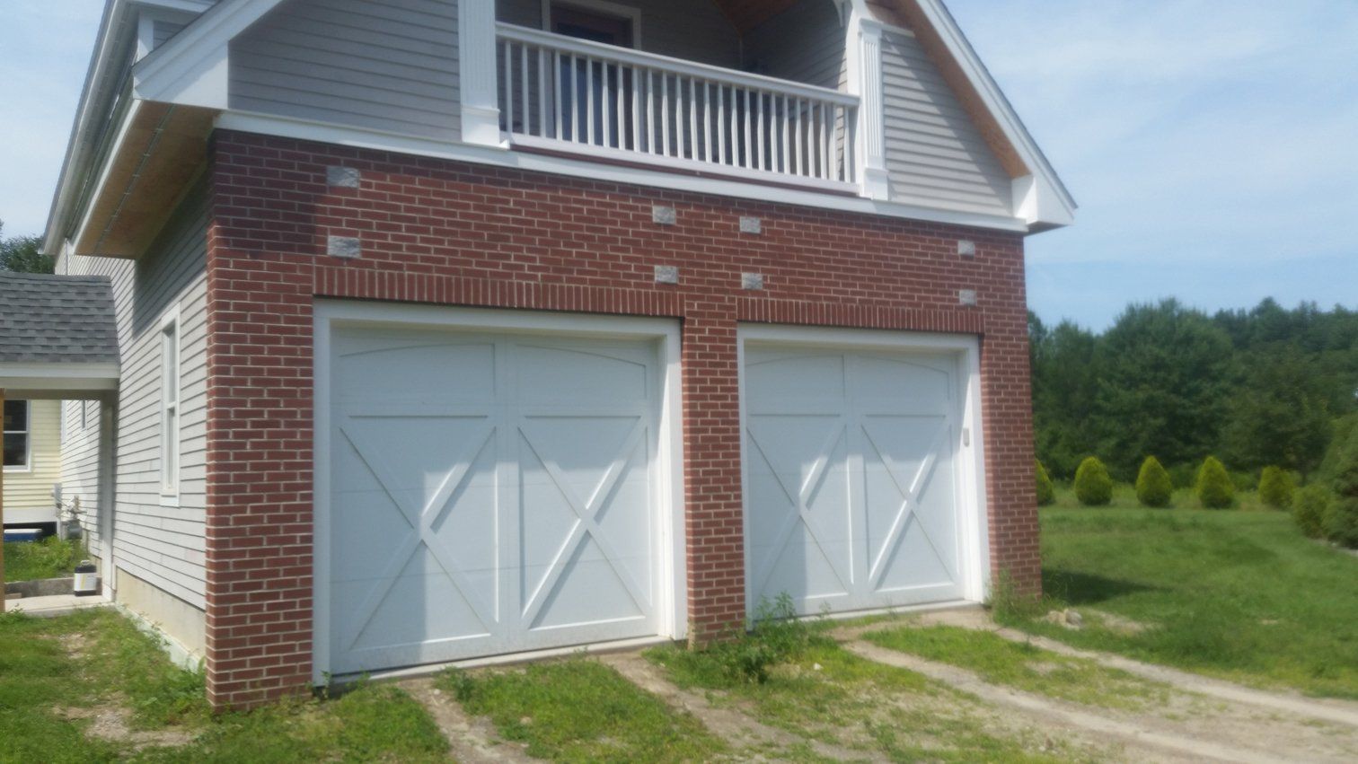 Two-car garage with white doors, surrounded by red brick, with an upper story balcony.