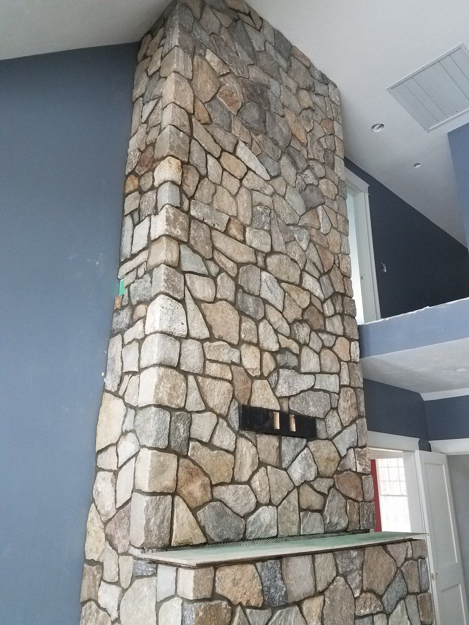 Stone fireplace with neutral-colored stones against blue and white walls, with a rectangular opening.