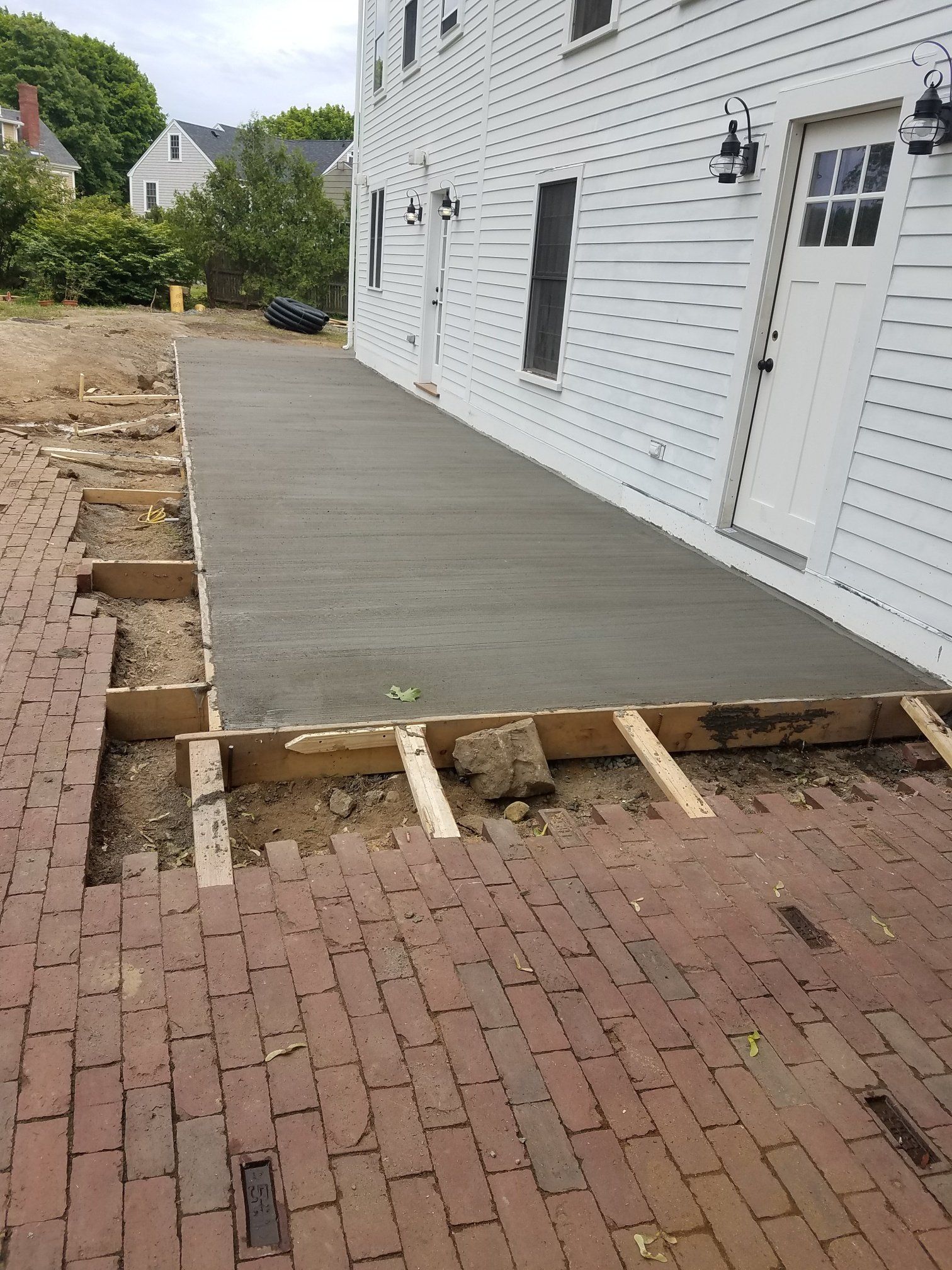 Newly poured concrete patio next to a white building. Old brick pavers border the patio.