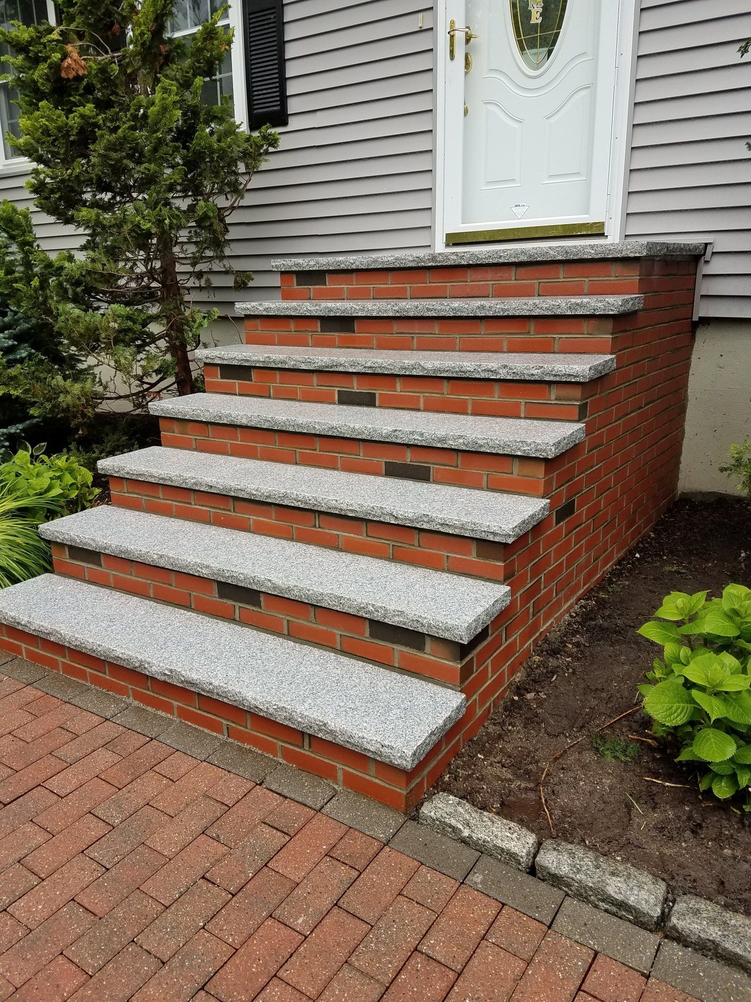 Brick stairs leading to a white door. The steps are gray, with brick risers. Red brick paving in front.