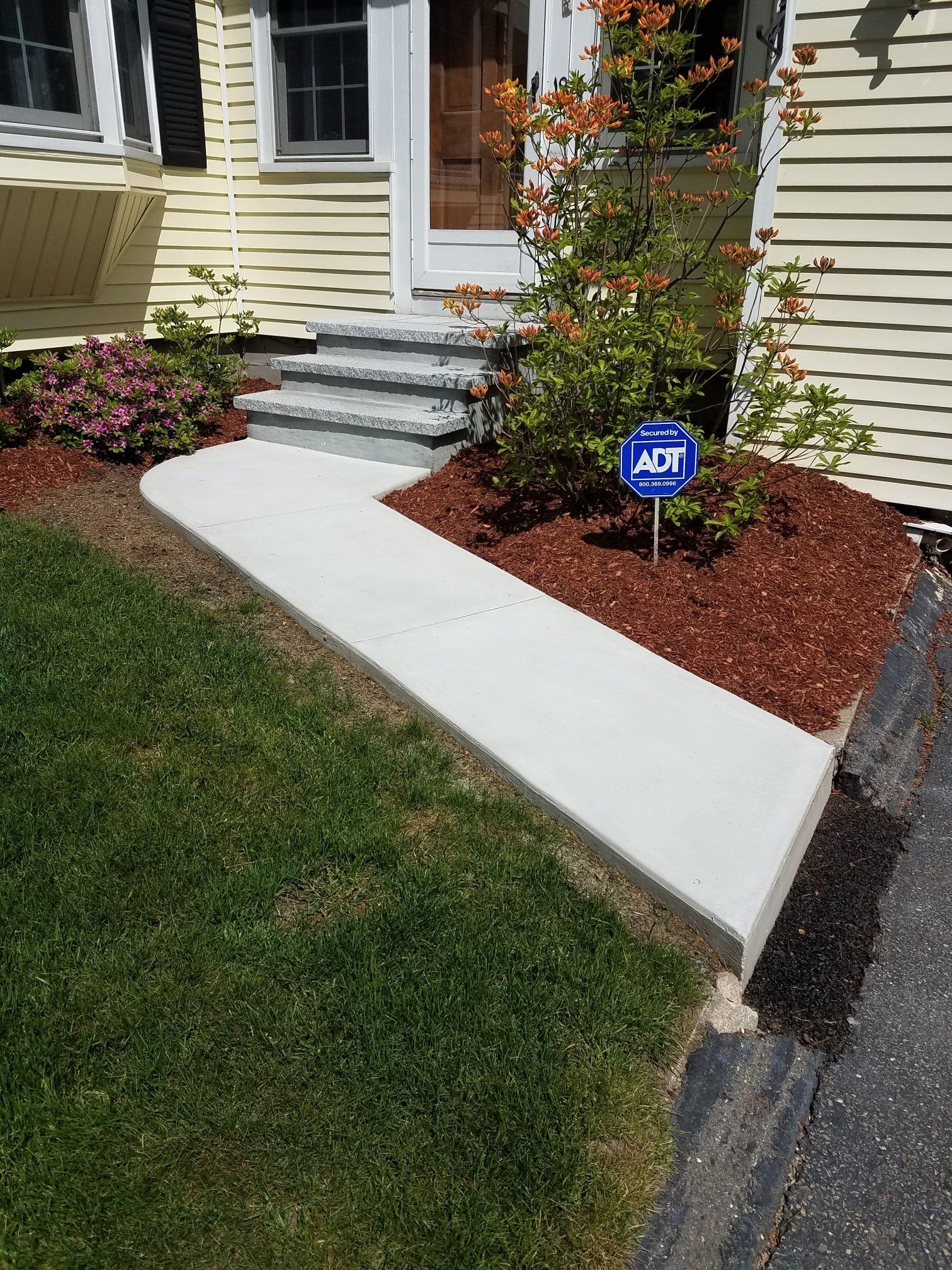 Concrete walkway leading to a house entrance with steps and a security sign.