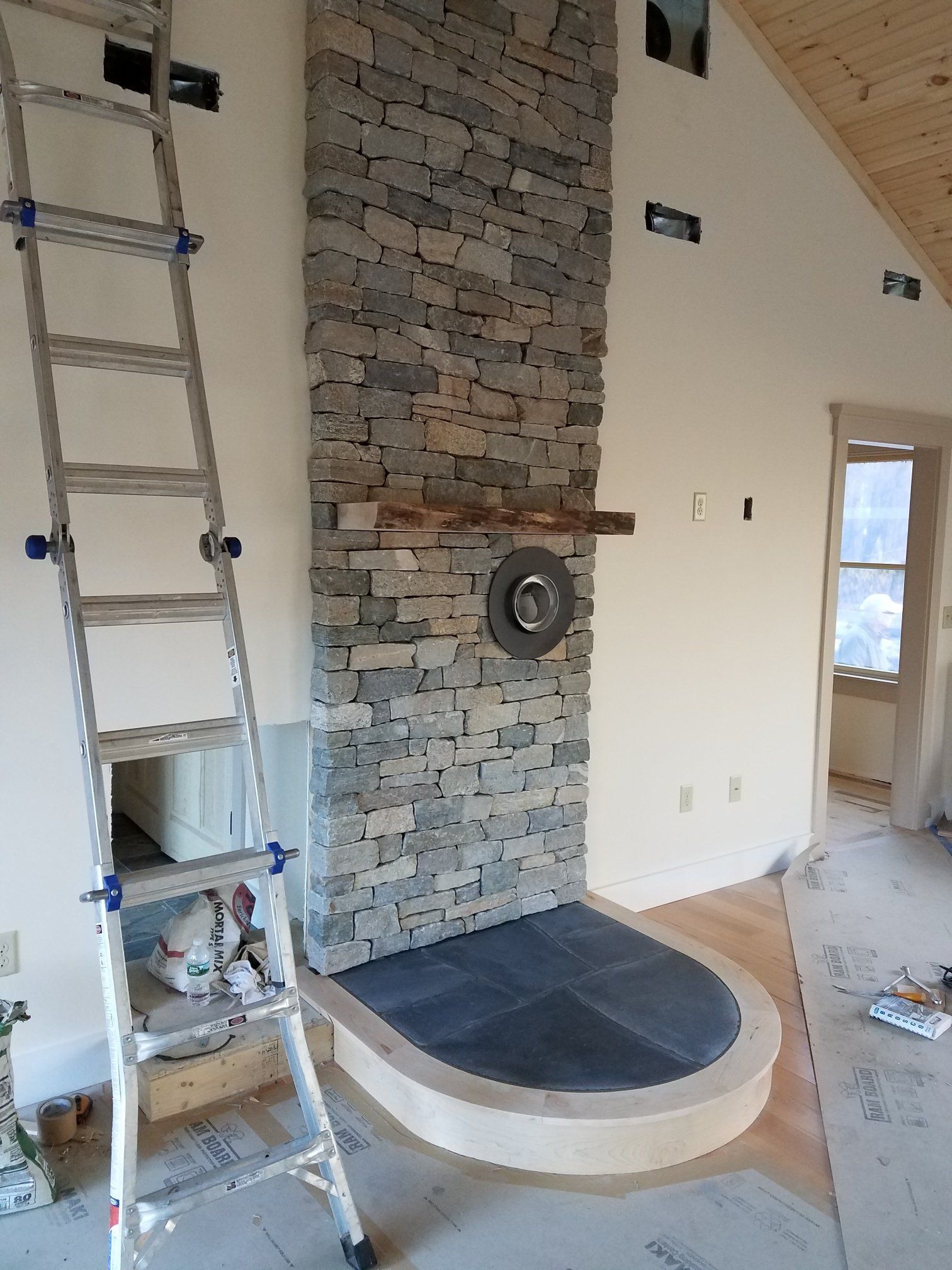 Ladder leaning against a stone fireplace under construction. The hearth has a curved border.