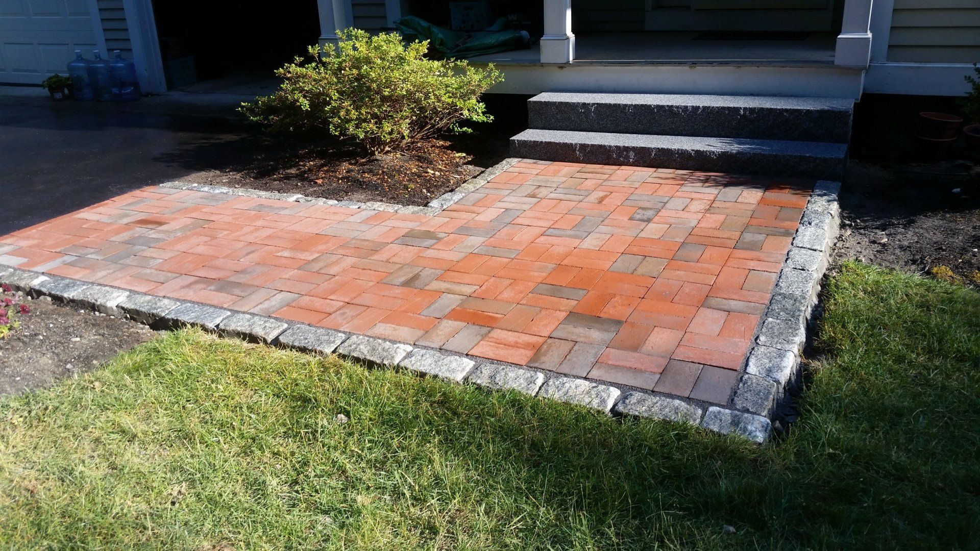 Brick pathway leading to steps and entrance of a house, bordered by grey stones and green grass.