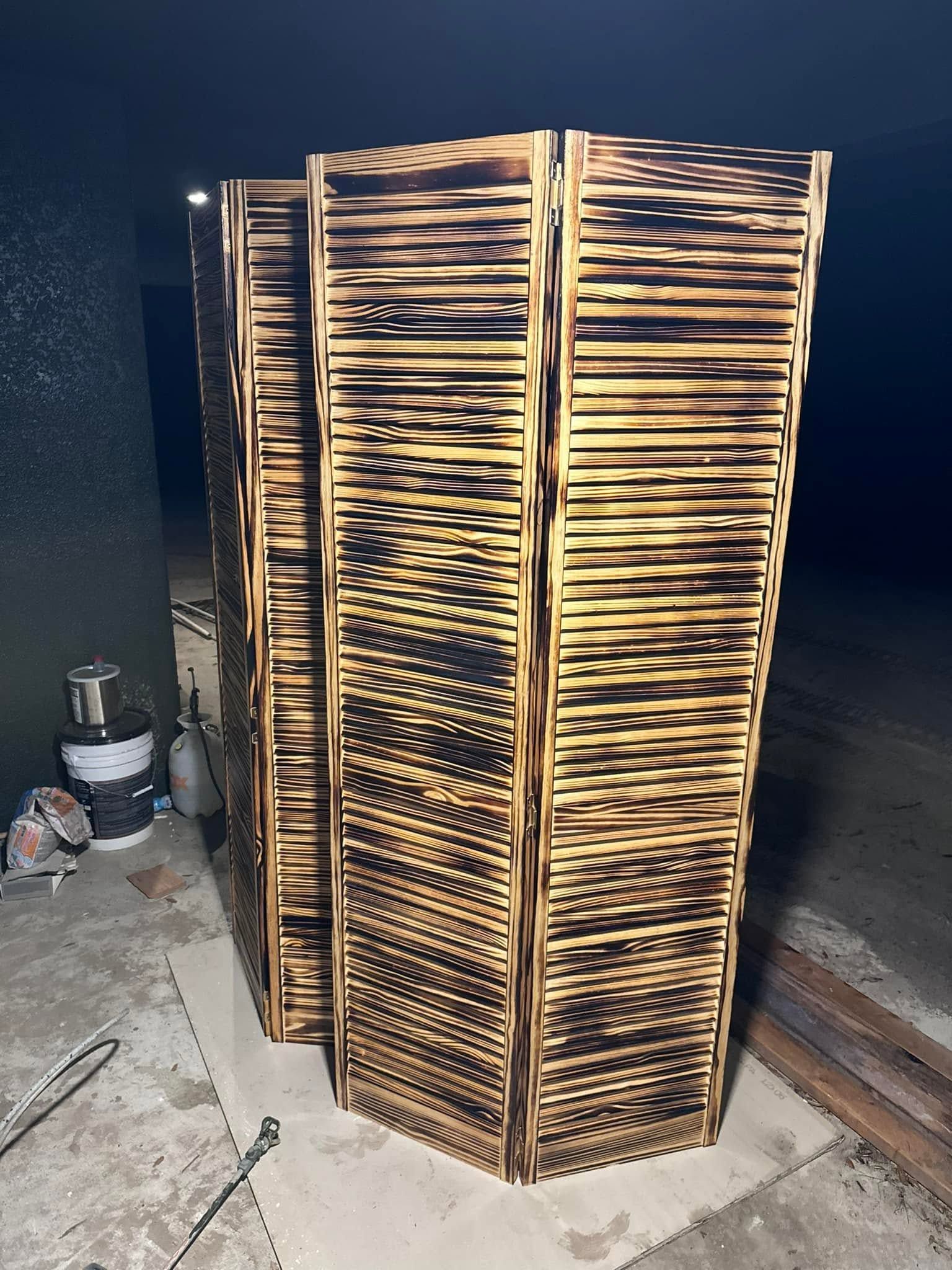 Tall woven wooden room divider with a zigzag pattern, standing on a concrete floor in a dim indoor space