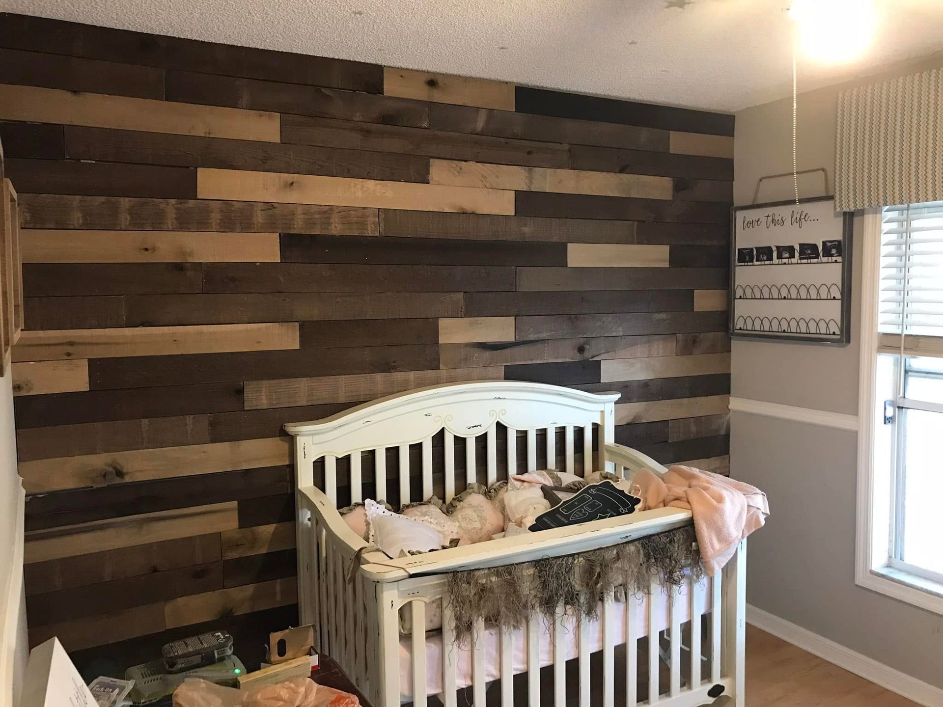 Crib in a nursery with a dark wood accent wall and a window letting in daylight