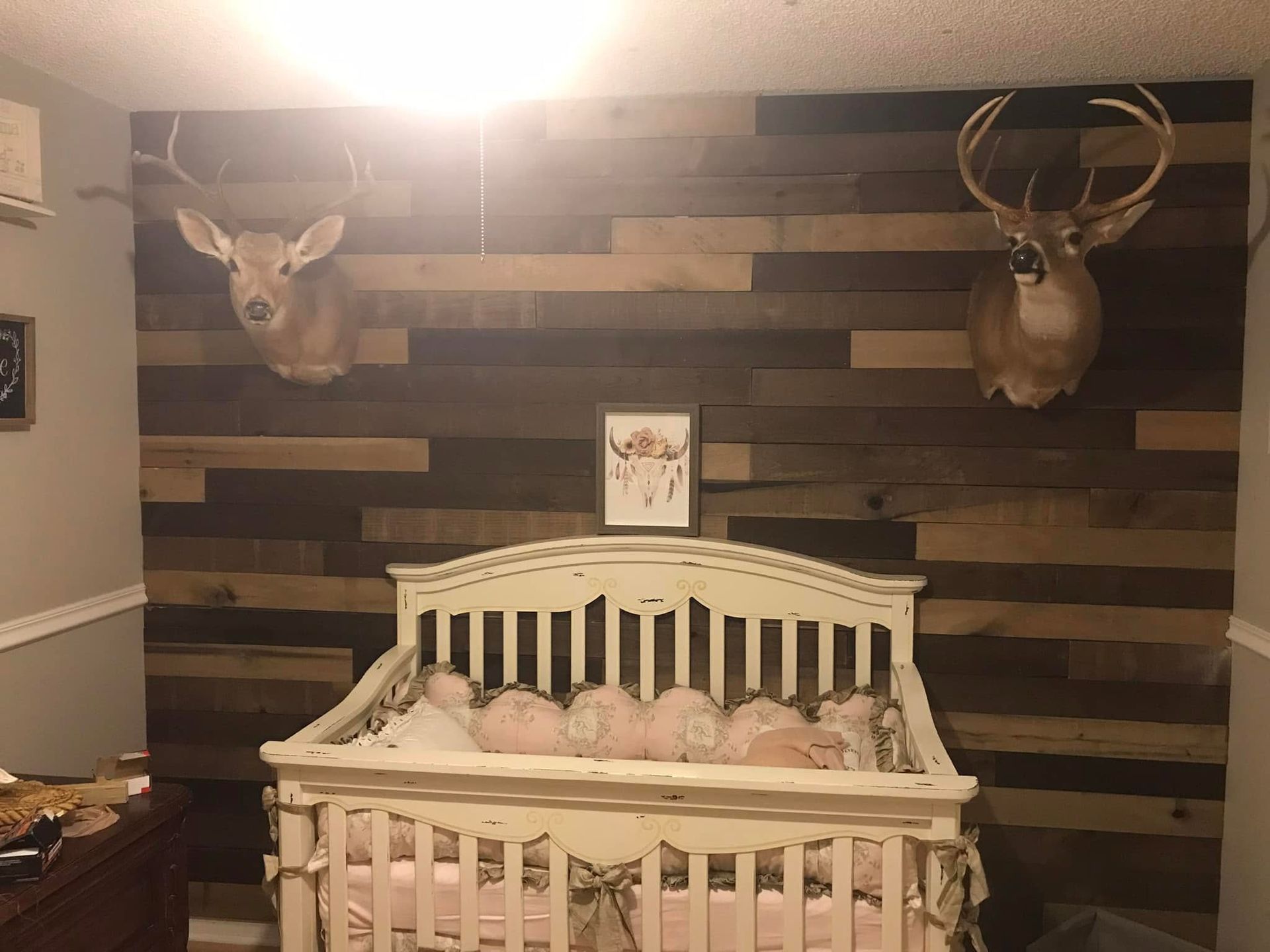 White crib in rustic nursery with deer mounts on wood plank wall and warm ceiling light