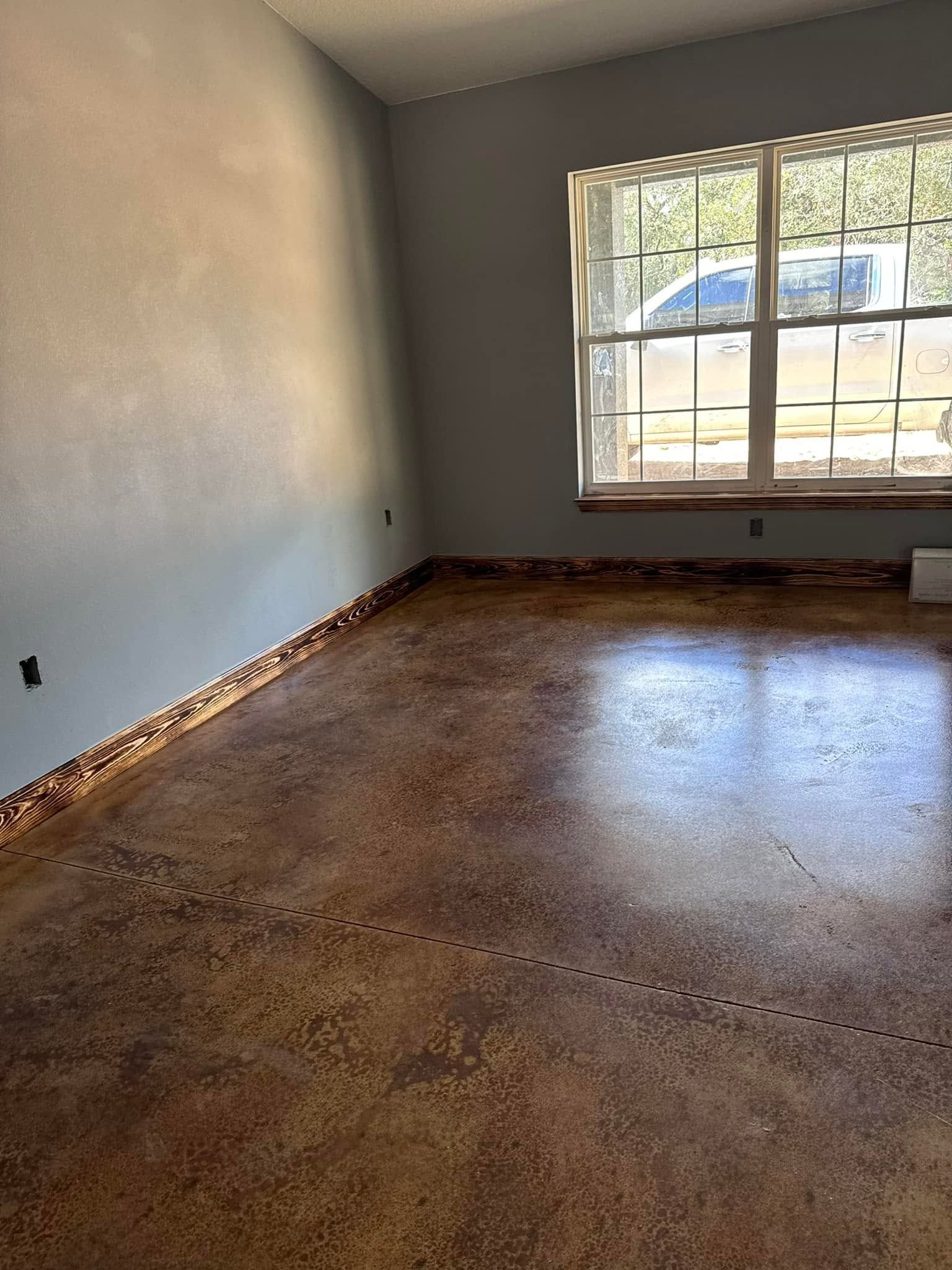 Empty room with brown floor, white walls, and a large window with bars and a blue awning outside