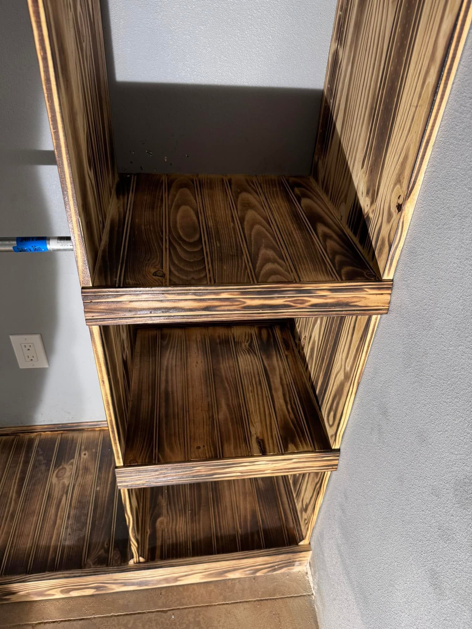 Open wooden shelving unit with three empty shelves and woven side panels in a room.