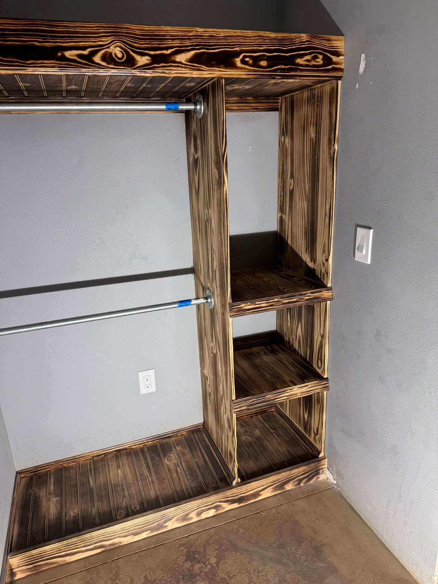Wooden closet shelving unit with three cubbies and hanging rods against a gray wall.