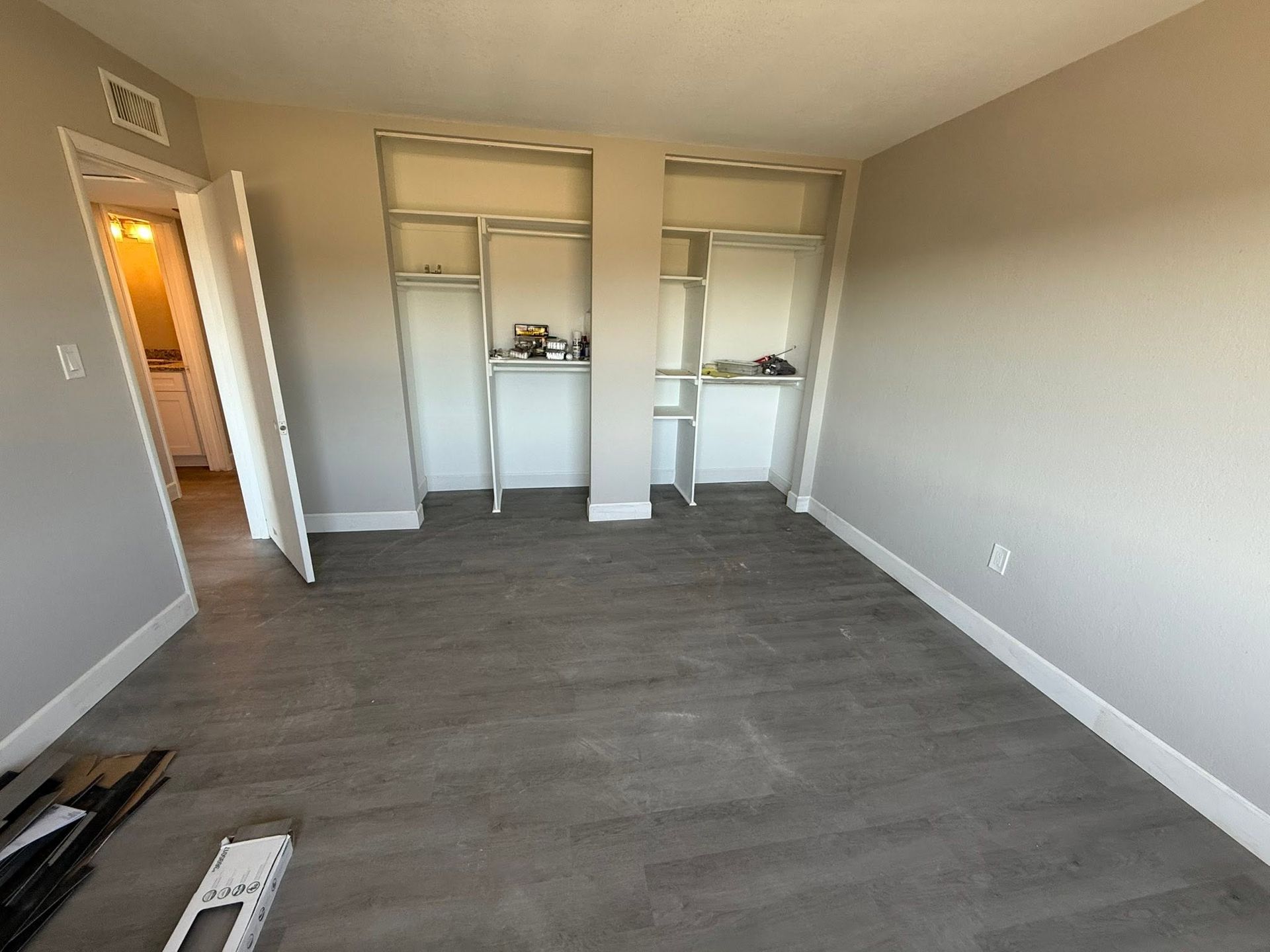 Empty beige bedroom with gray wood flooring and built-in closet shelves.