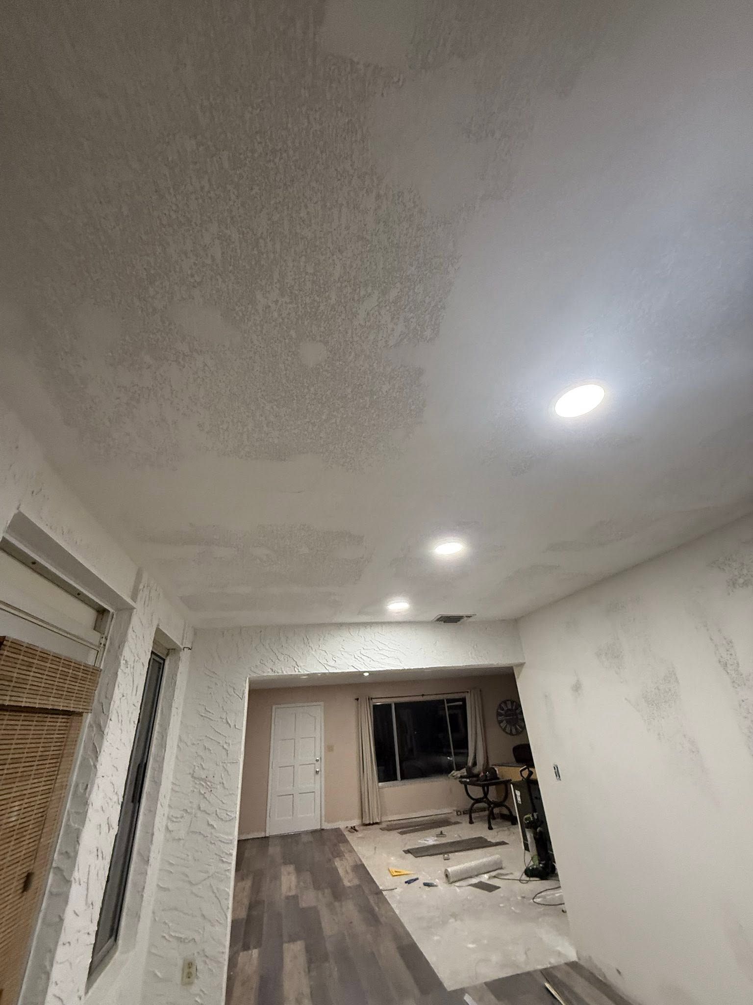 Long living room with patterned ceiling, recessed lights, and renovation materials on the floor