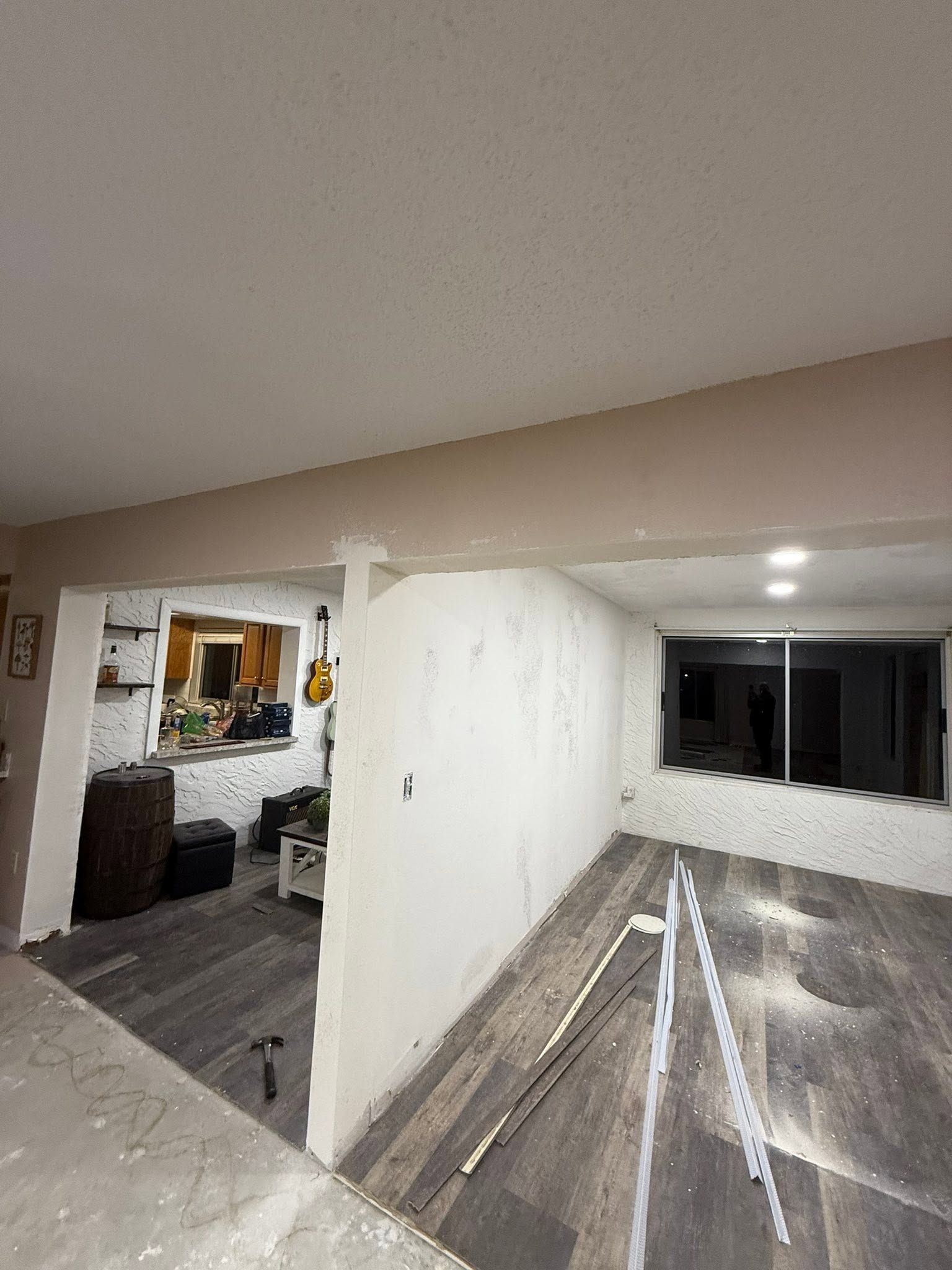 Interior room under renovation with white walls, exposed flooring, and a doorway to a living area.