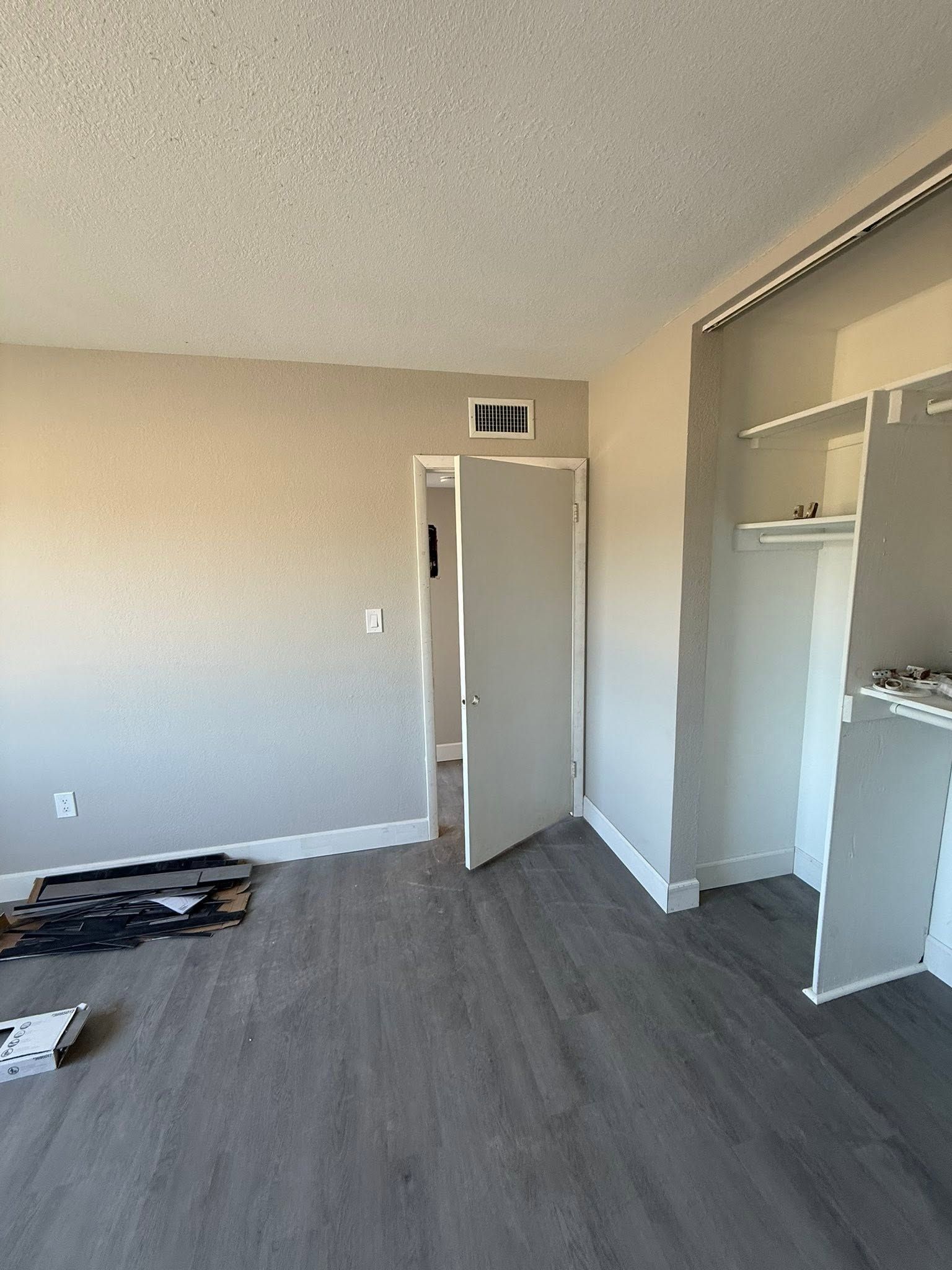 Empty beige bedroom with gray flooring, open closet, and partially open door to hallway