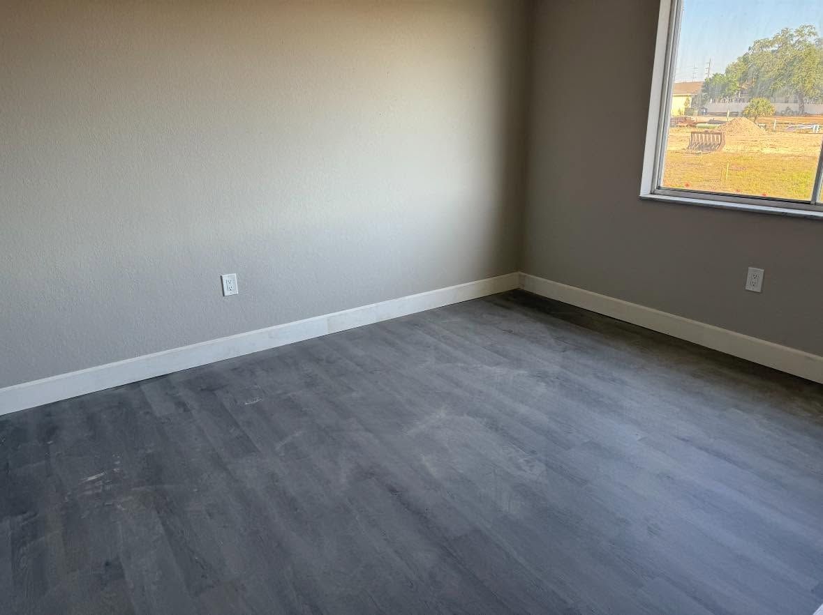 Empty room with gray walls, dark wood floor, and a window letting in daylight