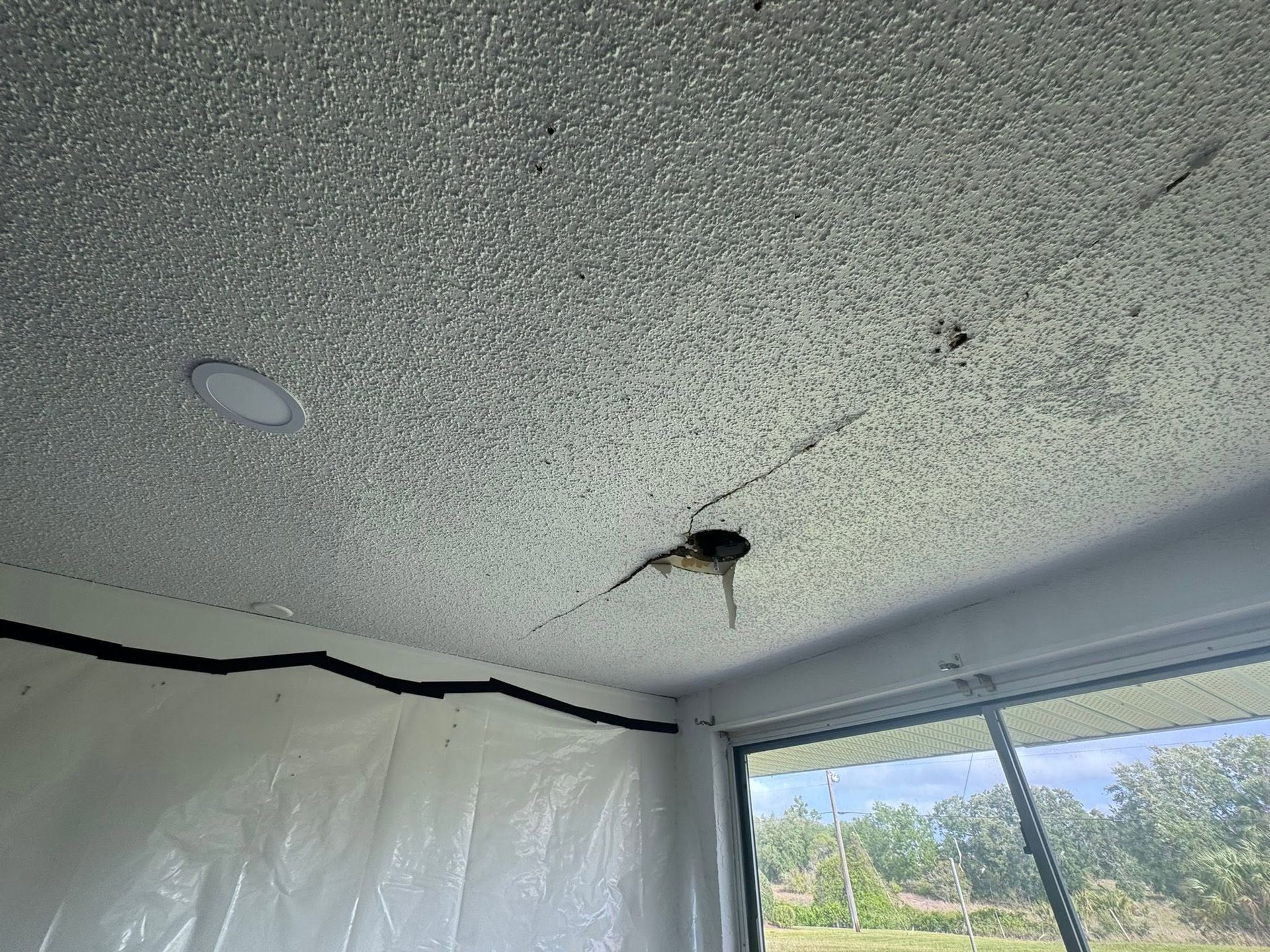 Damaged tent ceiling with a tear and hanging wiring, showing trees and sky through the opening