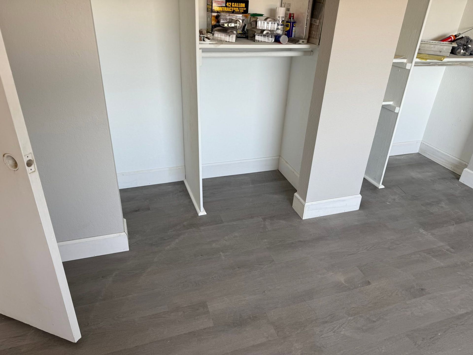 Empty room with gray wood flooring and white built-in closet shelves.