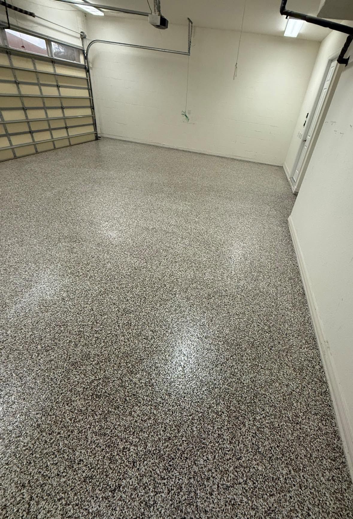 Empty garage with speckled epoxy floor, white walls, and shelves along the left side.