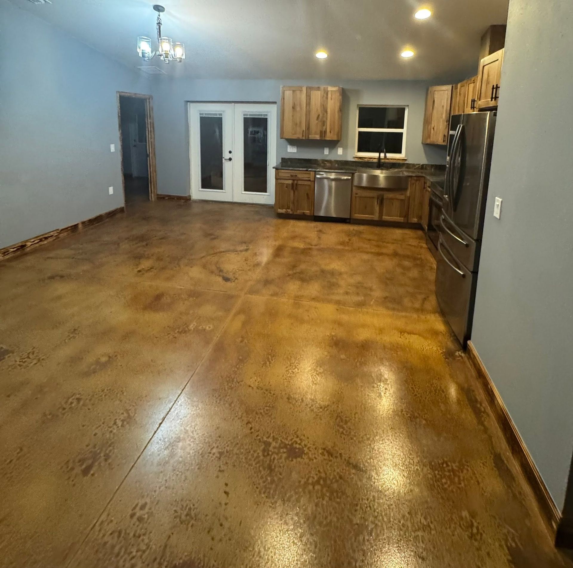 Empty kitchen with polished brown floors, wood cabinets, stainless appliances, and double French doors.