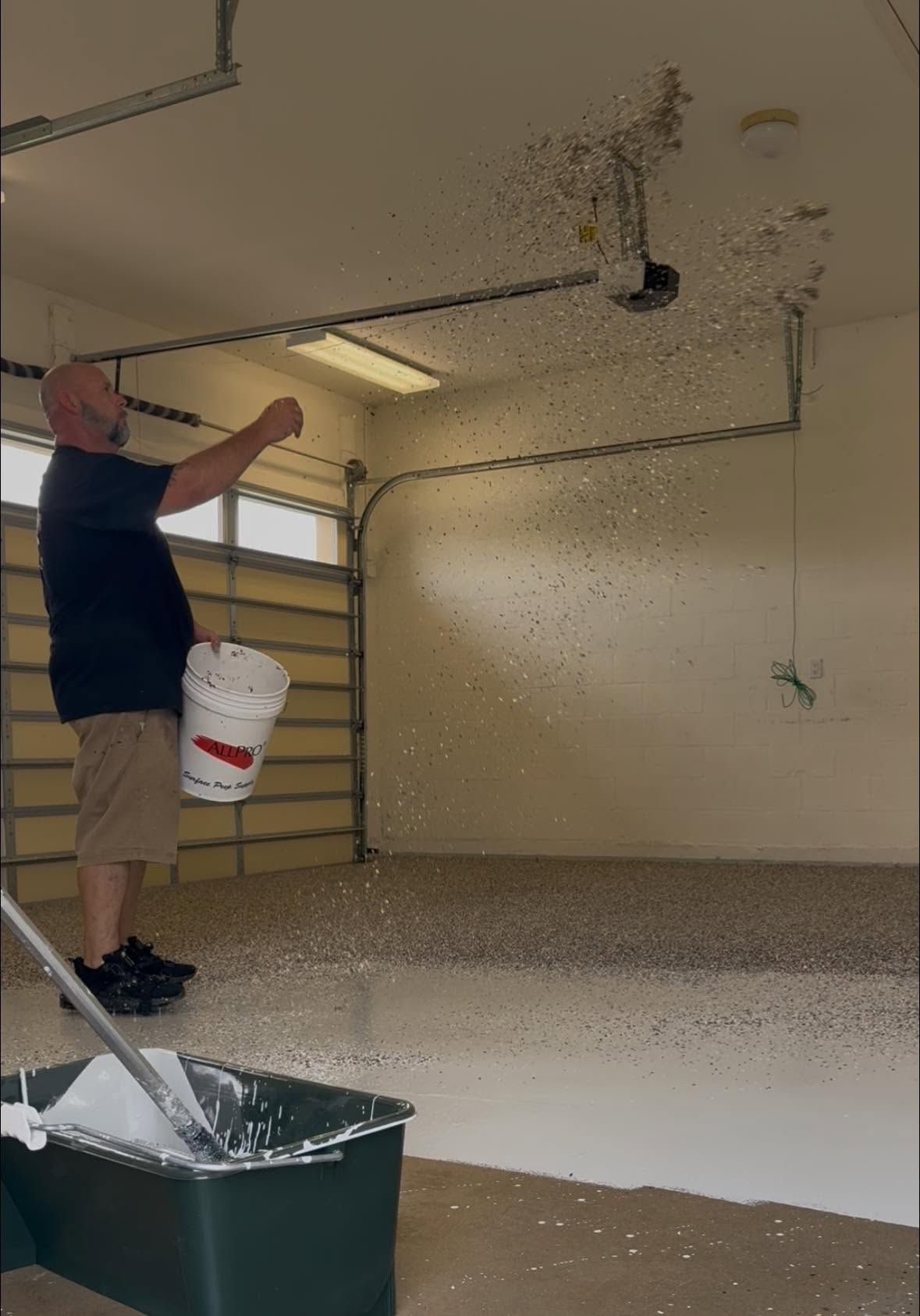 Person spraying white paint onto a garage ceiling and walls during a home improvement project