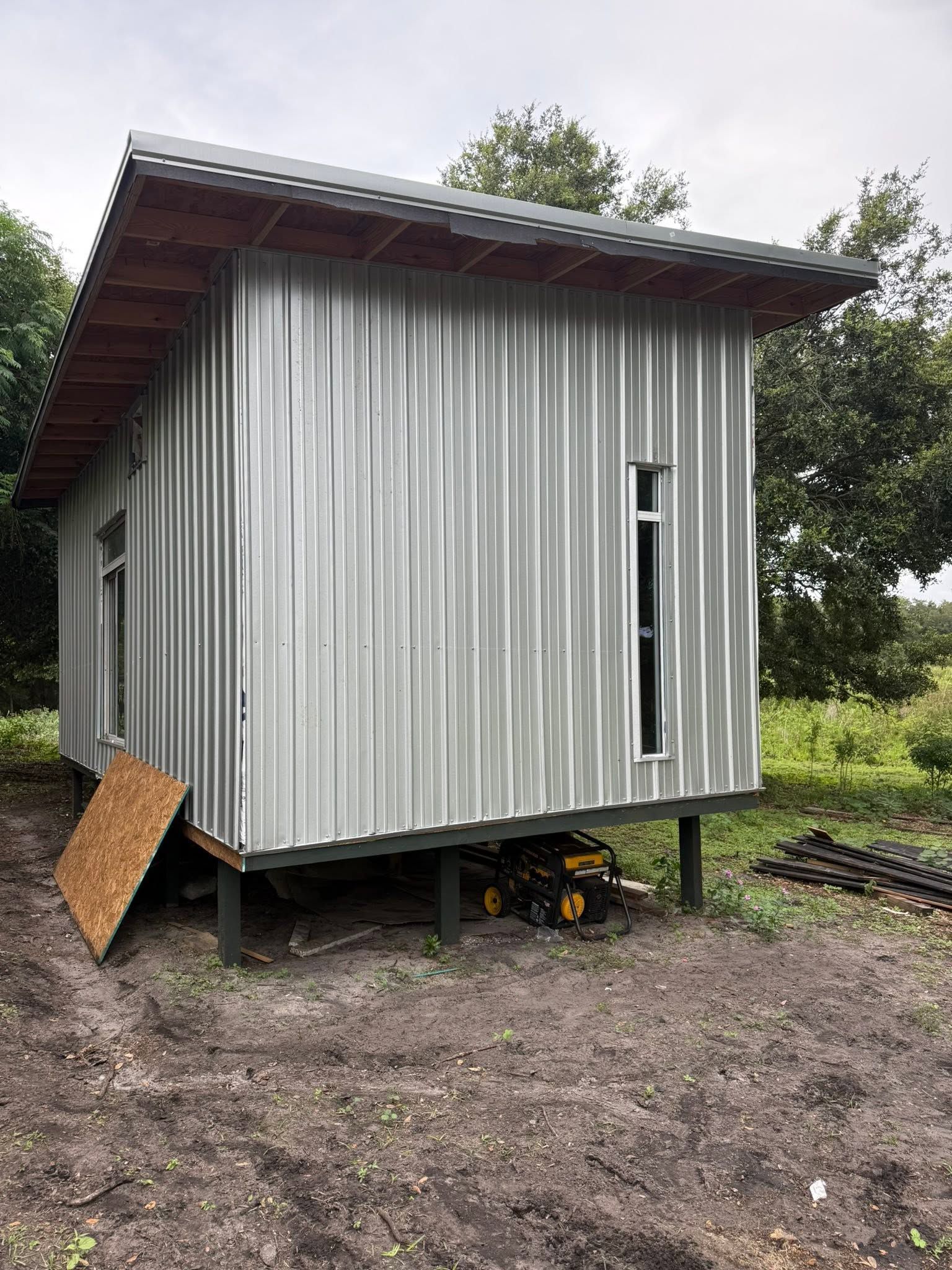 Small corrugated metal shed on stilts in a grassy, wooded area with a sloped roof and narrow window.
