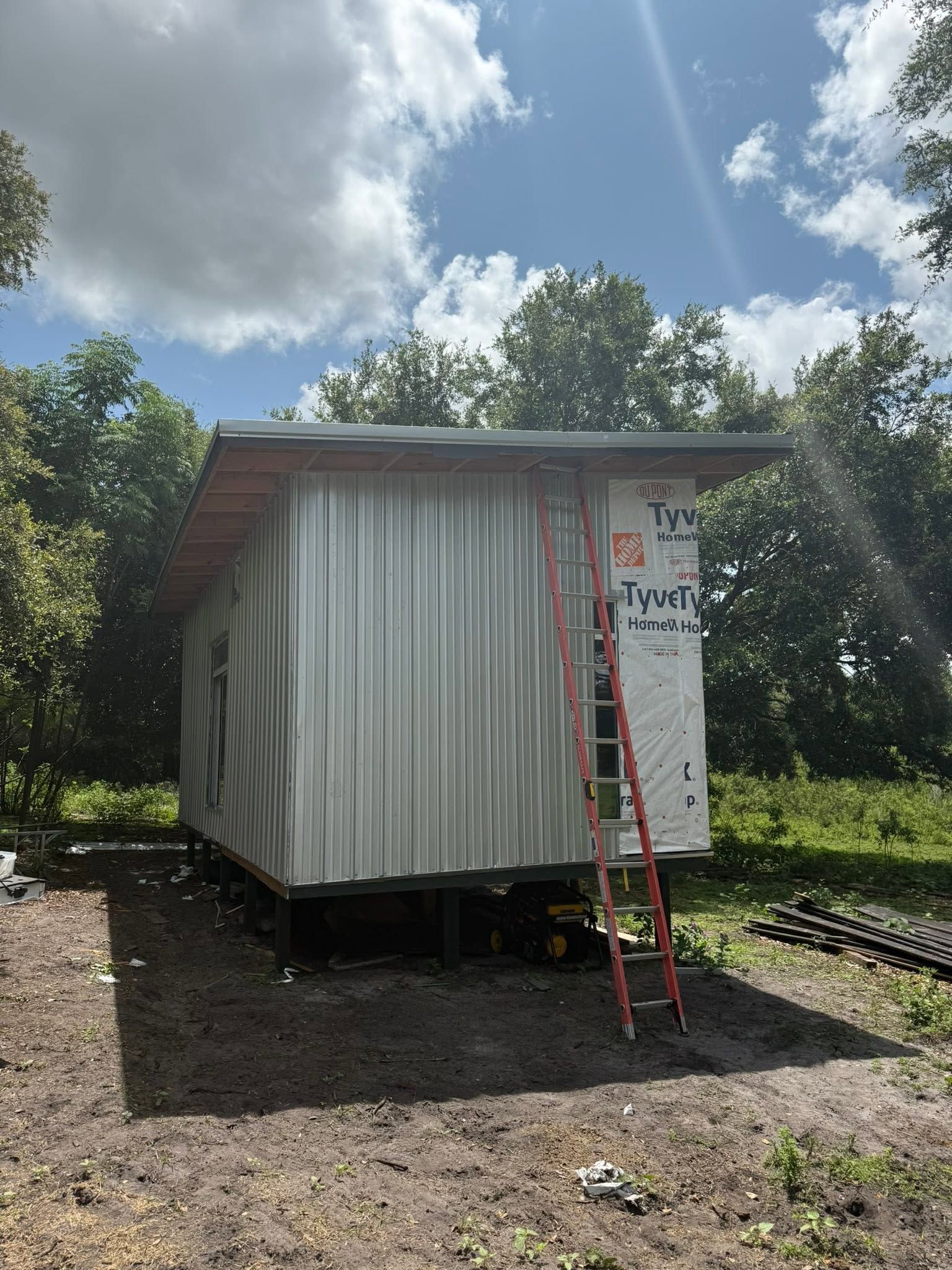 Small white shed on blocks with a red ladder leaning against it, under a sunny blue sky.