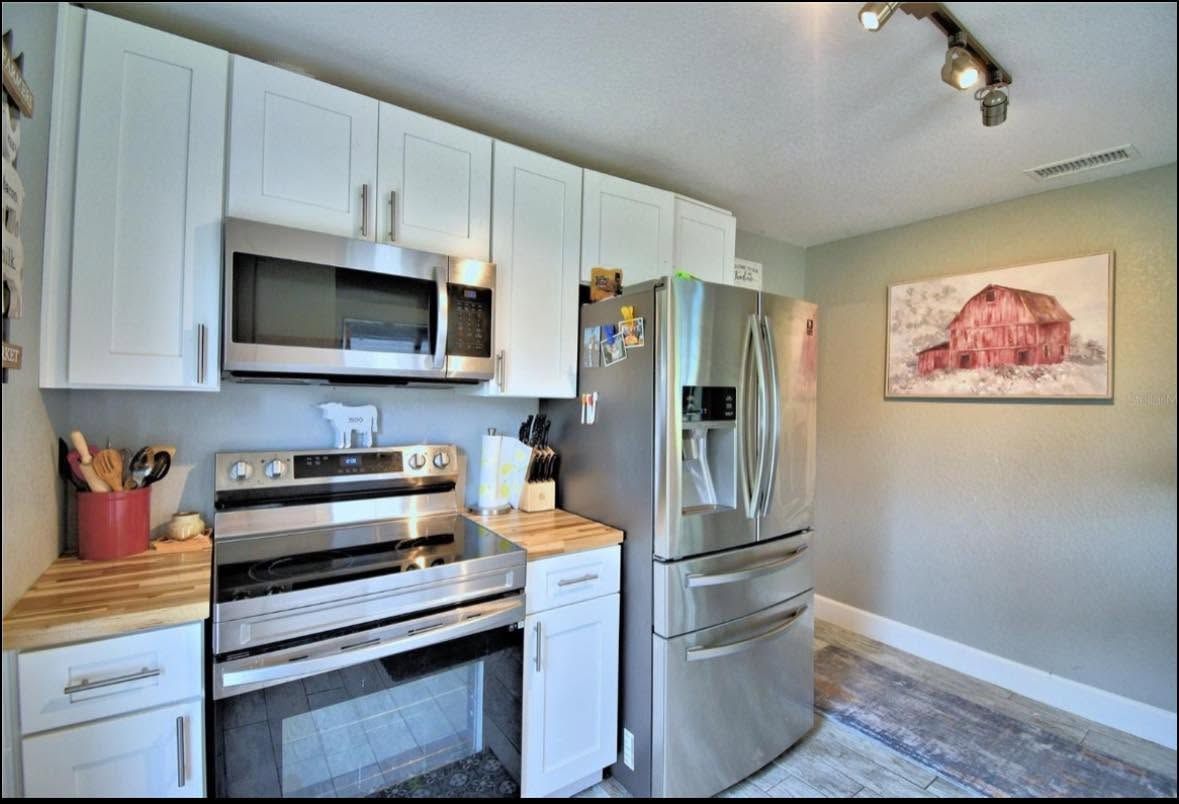 Bright kitchen with stainless steel appliances, white cabinets, wood countertops, and a pink wall art piece.