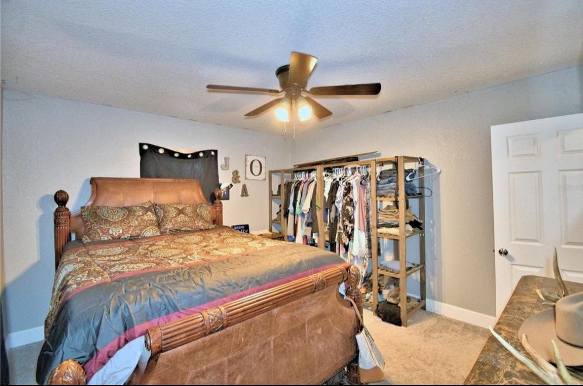Bedroom with a large bed, ceiling fan, shelving unit, and closed white closet doors