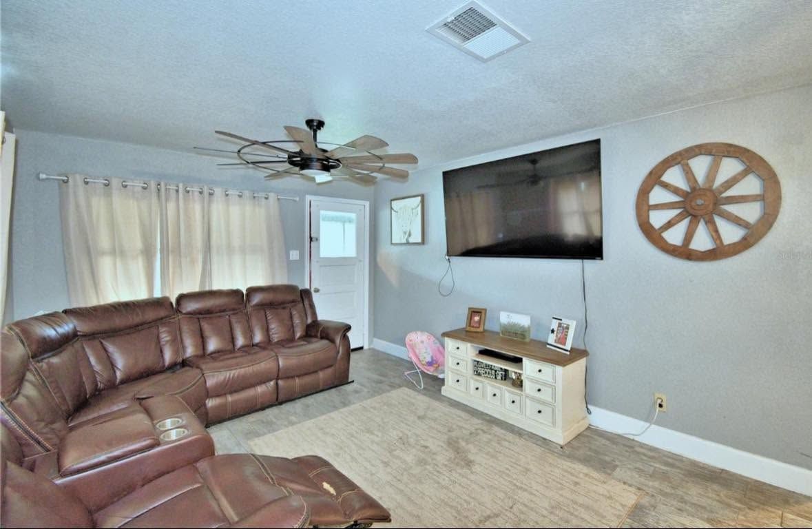 Living room with brown leather sectional, wall-mounted TV, beige rug, and decorative wheel wall art