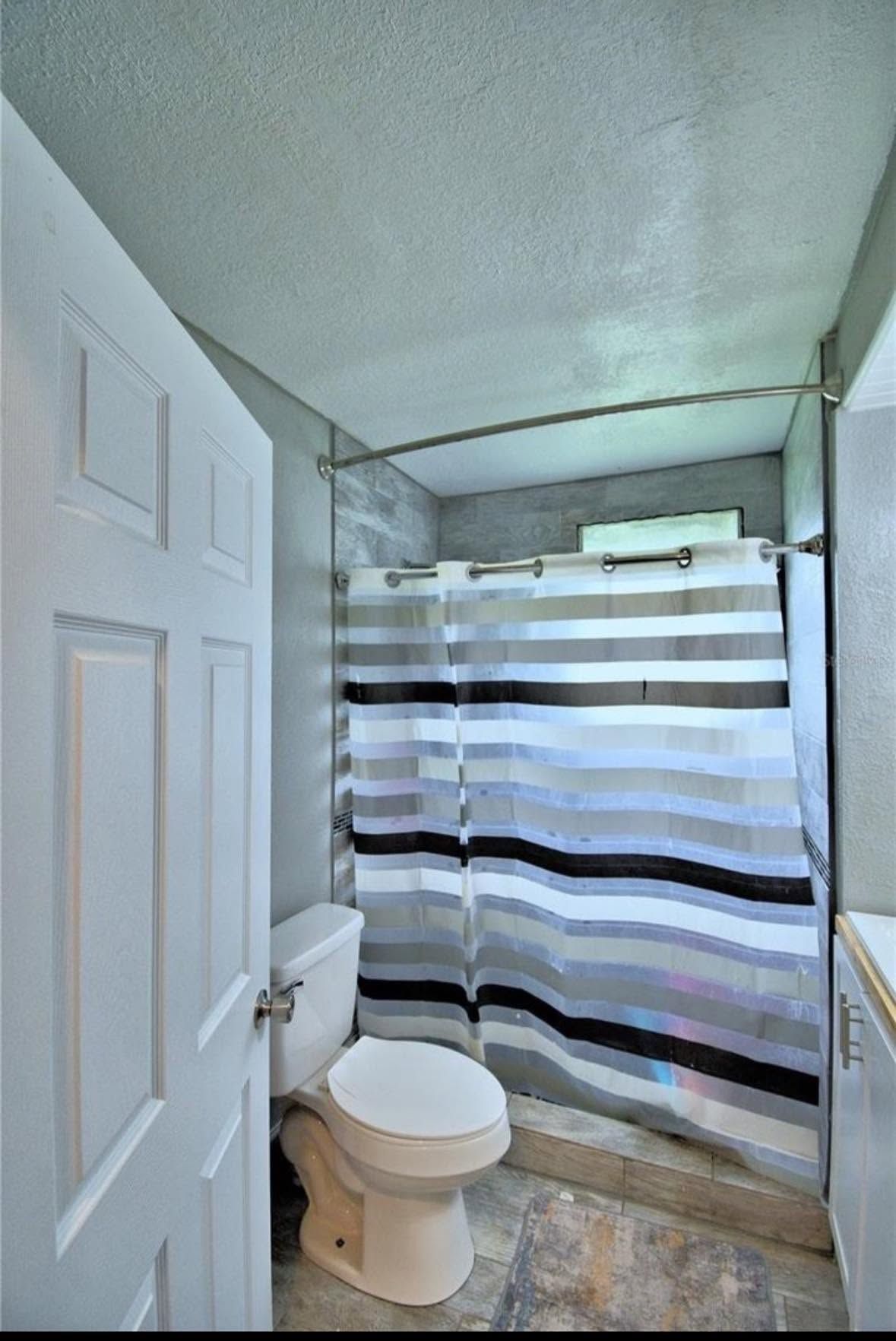 Small bathroom with toilet, shower curtain, and door; narrow space with gray walls and white ceiling.
