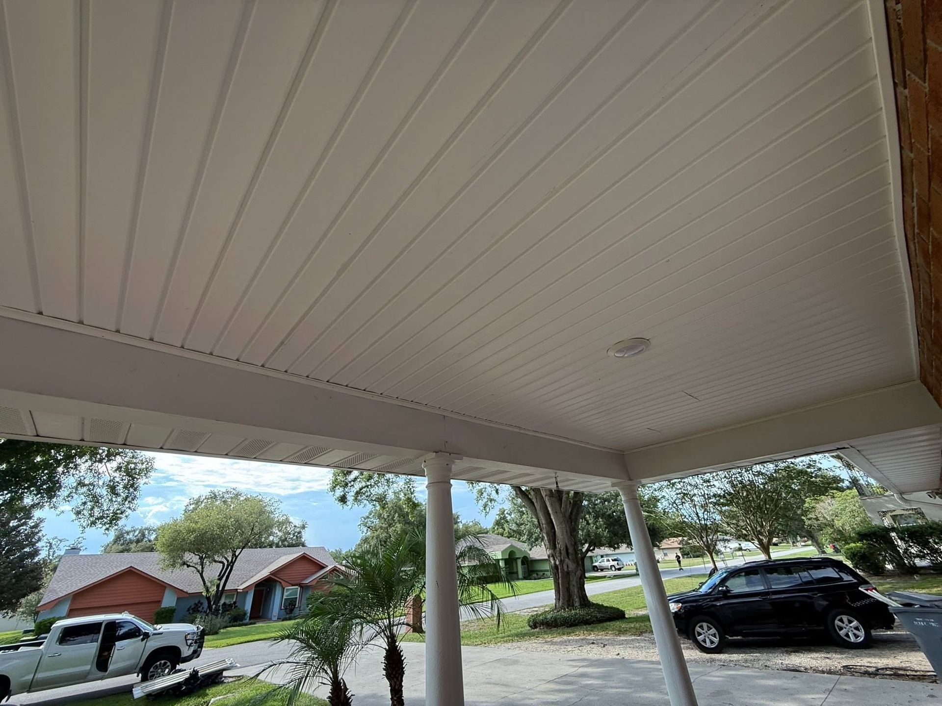 Covered porch overlooking a suburban street with parked cars and trees on a sunny day