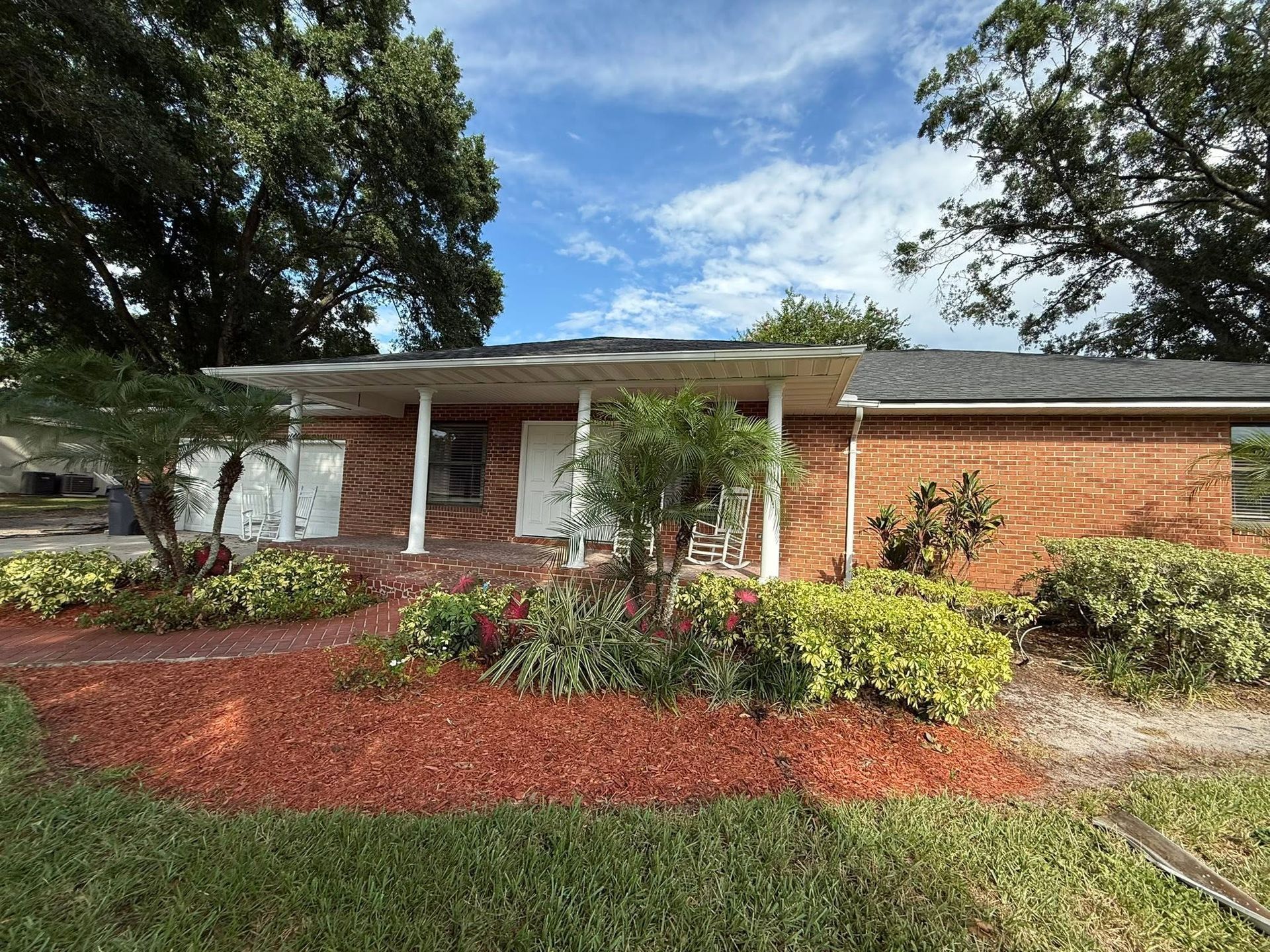 Single-story brick house with white trim, front porch, and landscaped yard under a blue sky