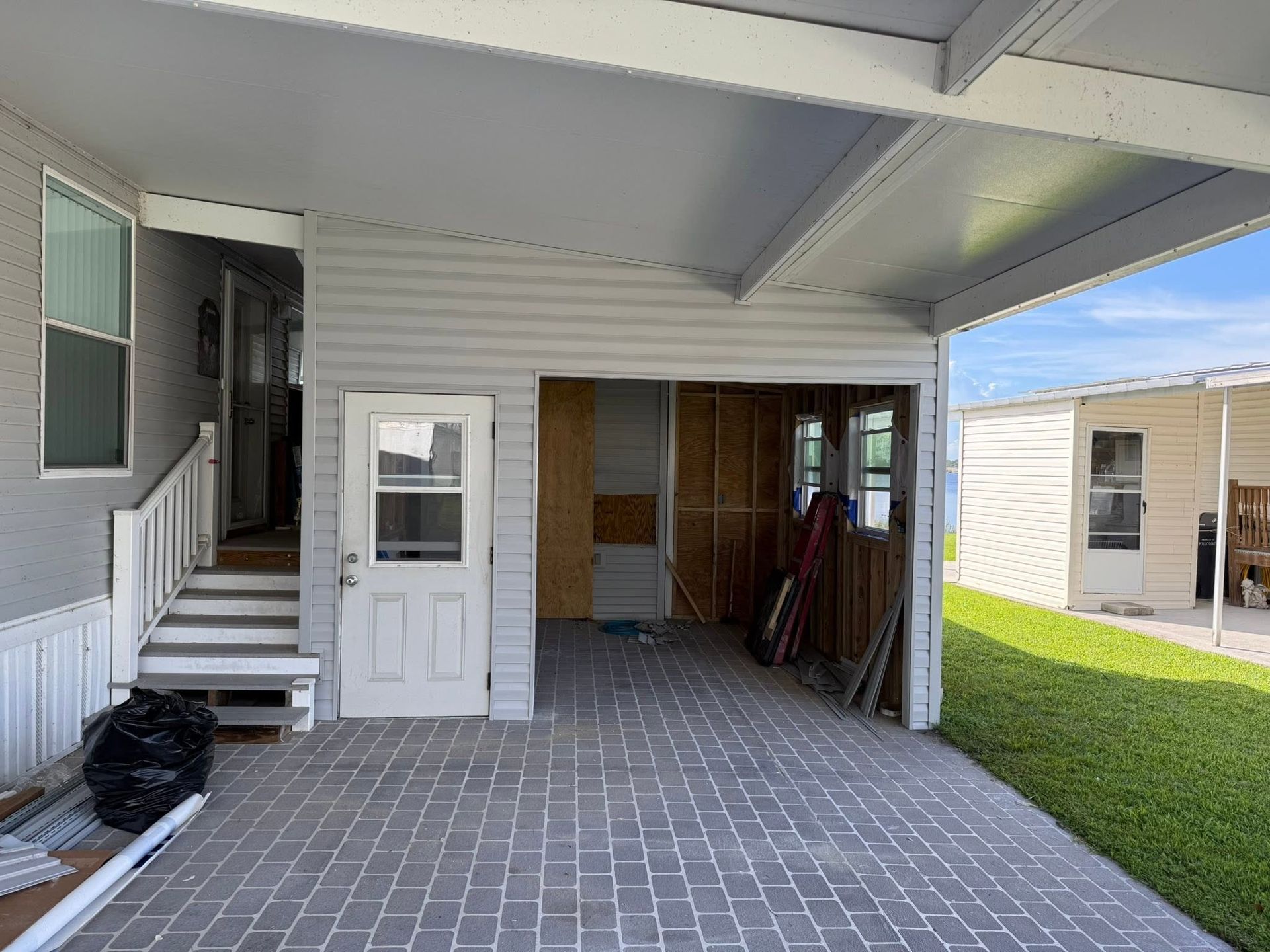 Covered patio with white stairs, a side door, and storage area beside a grassy yard.