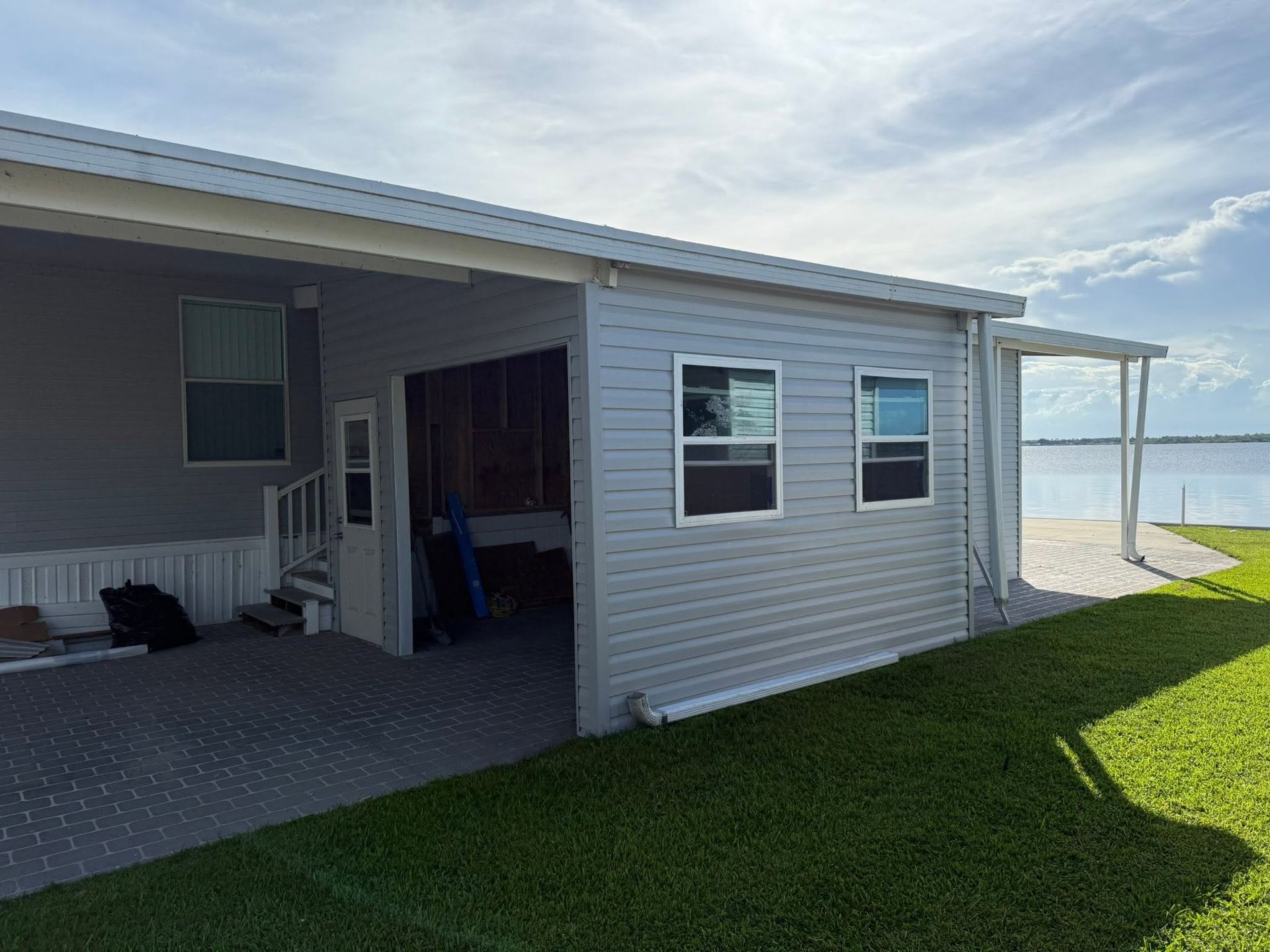 Covered patio of a beach house with gray siding, green lawn, and ocean visible in the background