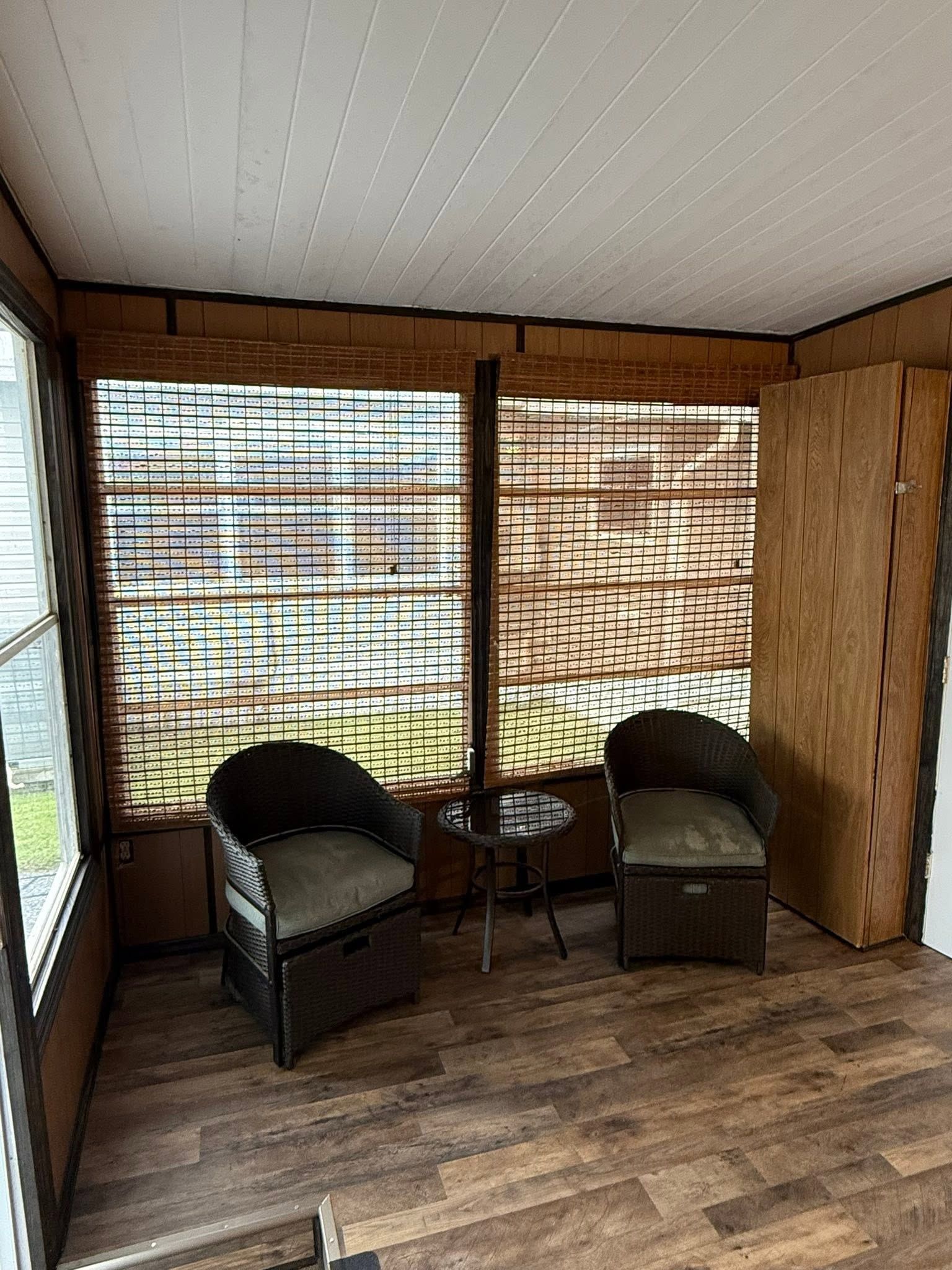 Small screened porch with two wicker chairs, a round table, and wood-paneled walls.