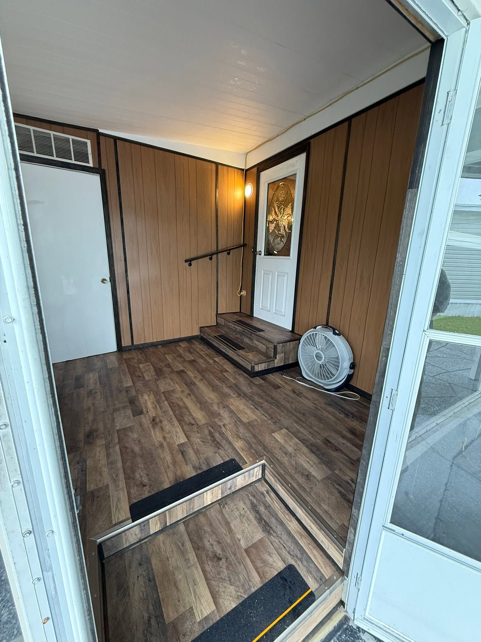 Covered front porch with wood-paneled walls, a white door, and steps leading down to the yard.