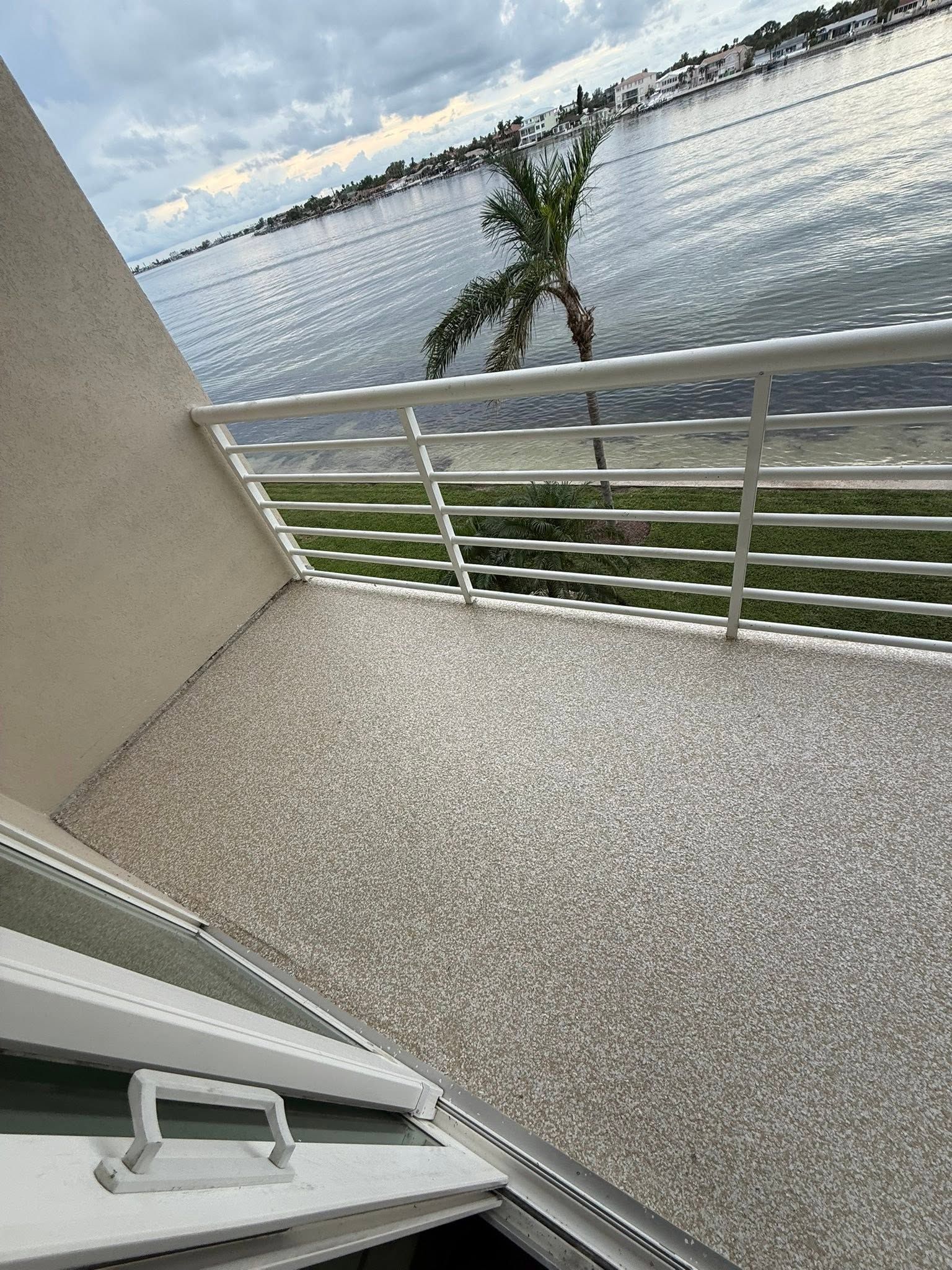 Balcony overlooking calm water with white railing and a small tree in the foreground