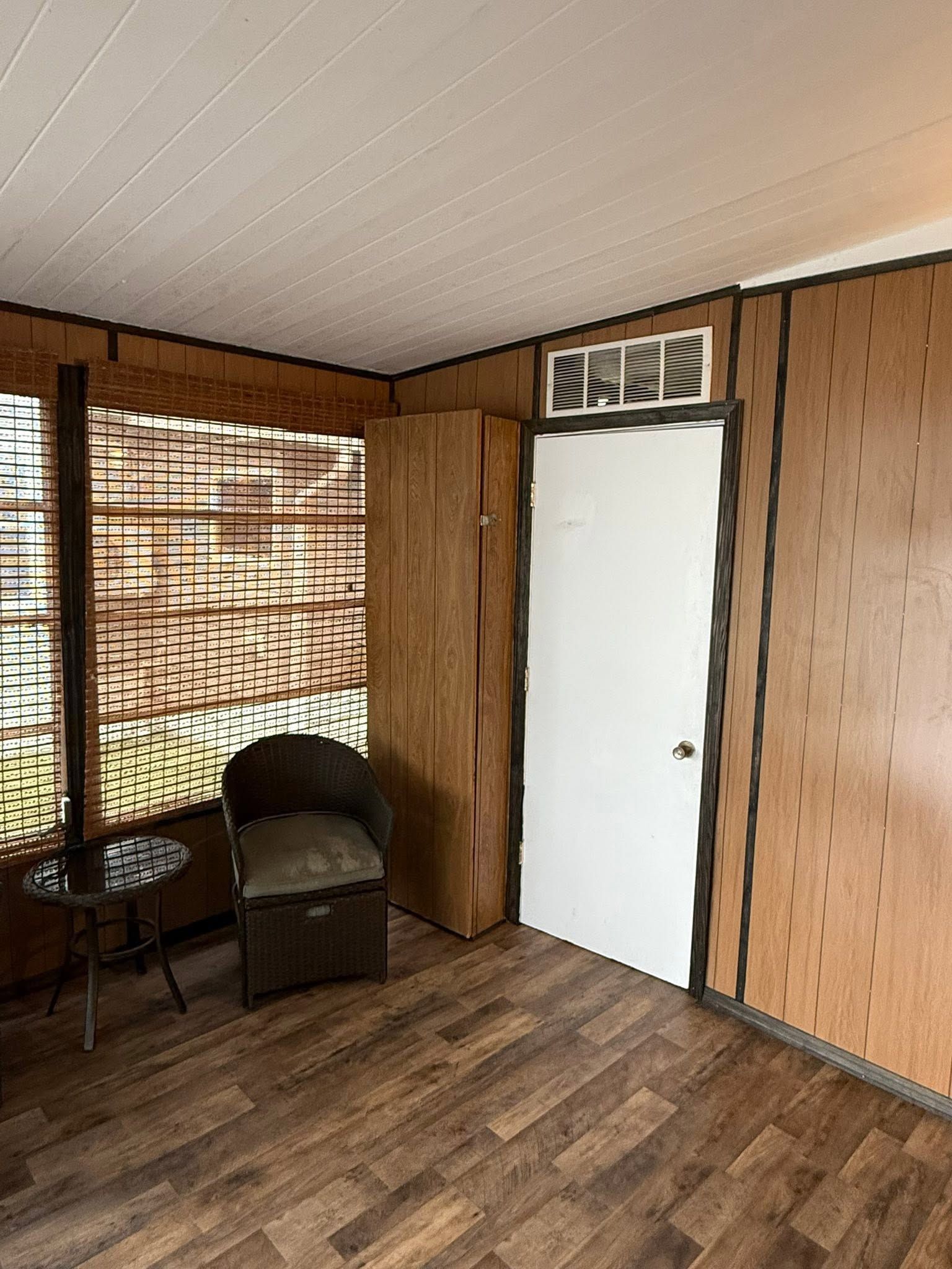 Small wood-paneled room with a chair, window blinds, and a white door with vents above it.