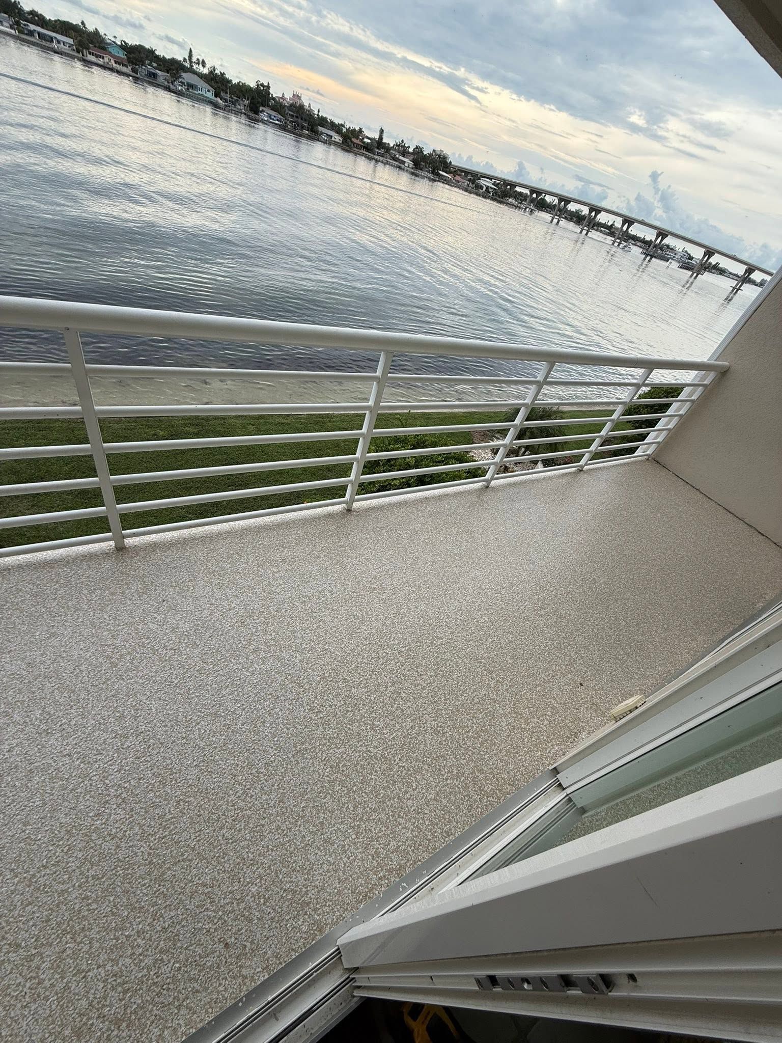 Riverside walkway with metal railing overlooking calm water and a distant shoreline at sunset